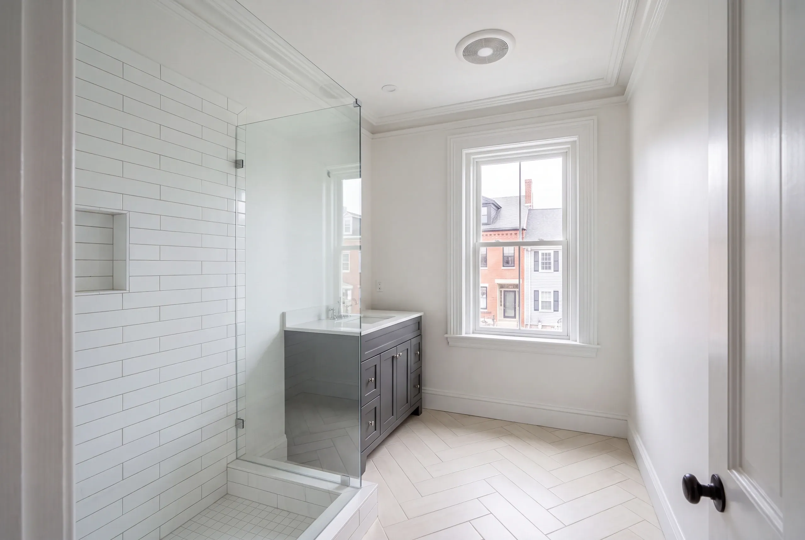 Bathroom remodeler Bath Maine: narrow bathroom with a glass subway tile shower, gray vanity and herringbone floor tile