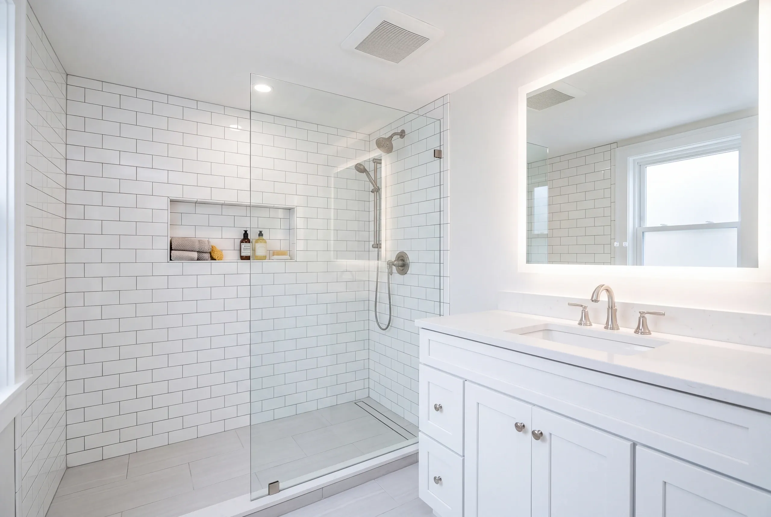 Bathroom renovation contractor Bath Maine: white bathroom with a subway tile walk-in shower, handheld spray and a large backlit mirror