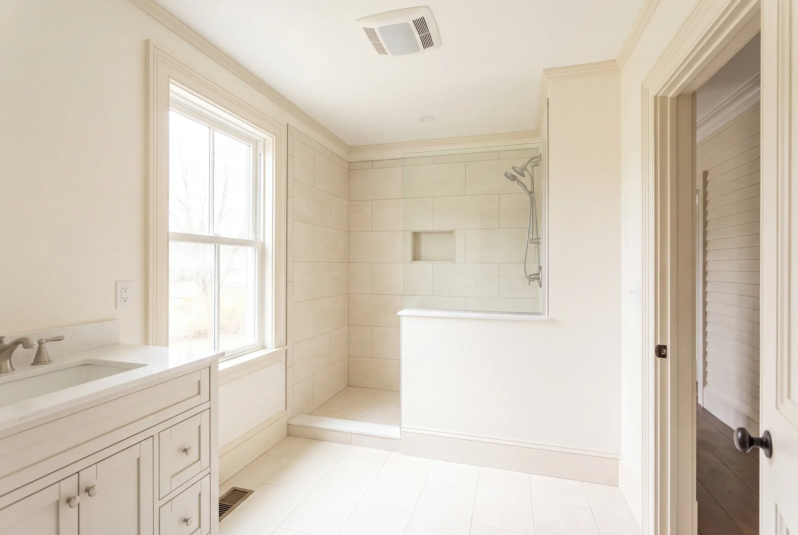 Bathroom remodeling in Belfast, ME: cream bathroom with a tiled walk-in shower behind a half wall and a cream shaker vanity