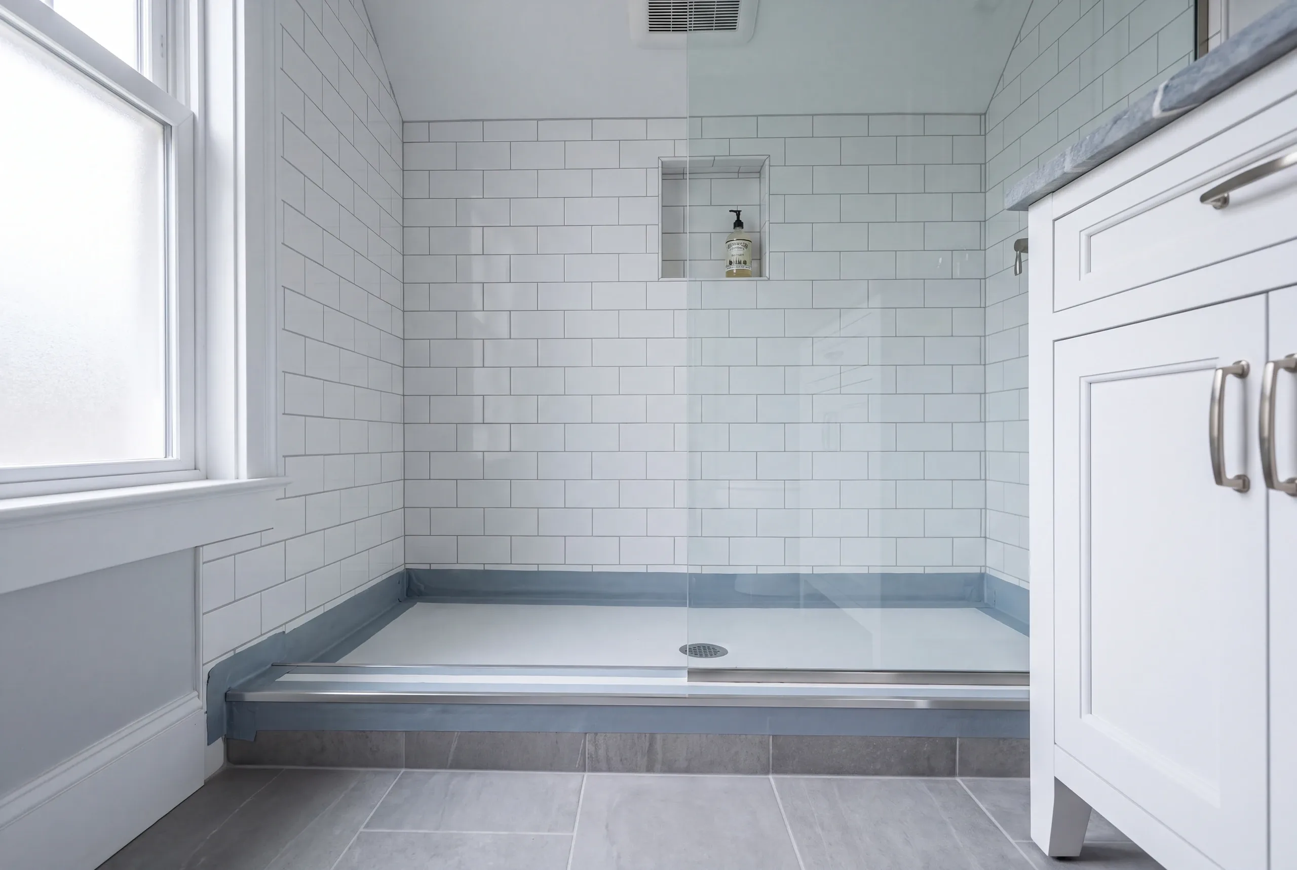 Bathroom renovation contractor Belfast Maine: subway tile shower with blue waterproofing membrane still showing along the pan and curb seams