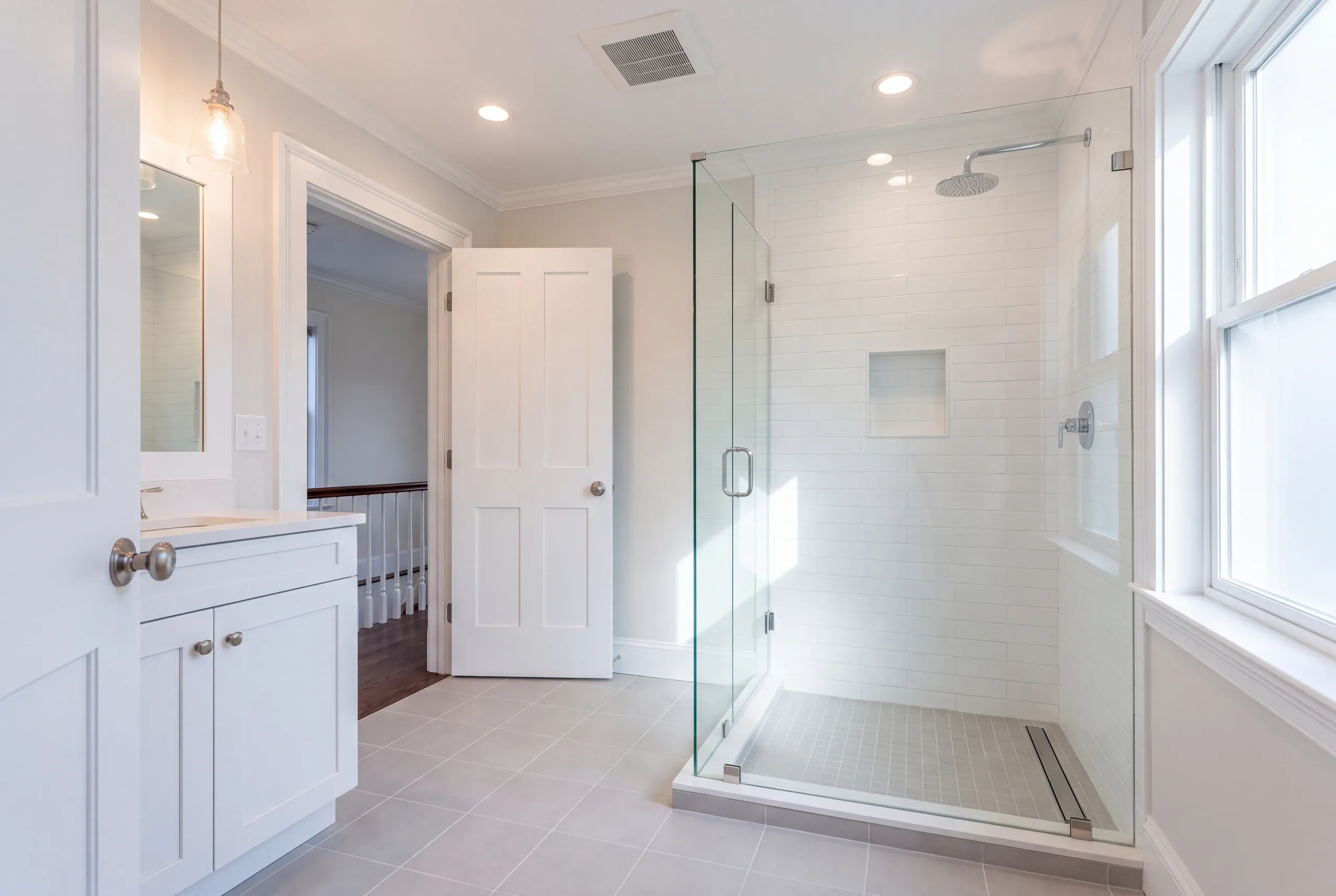 Bathroom remodeler Belfast Maine: frameless glass corner shower with a rain head and linear drain beside a white shaker vanity