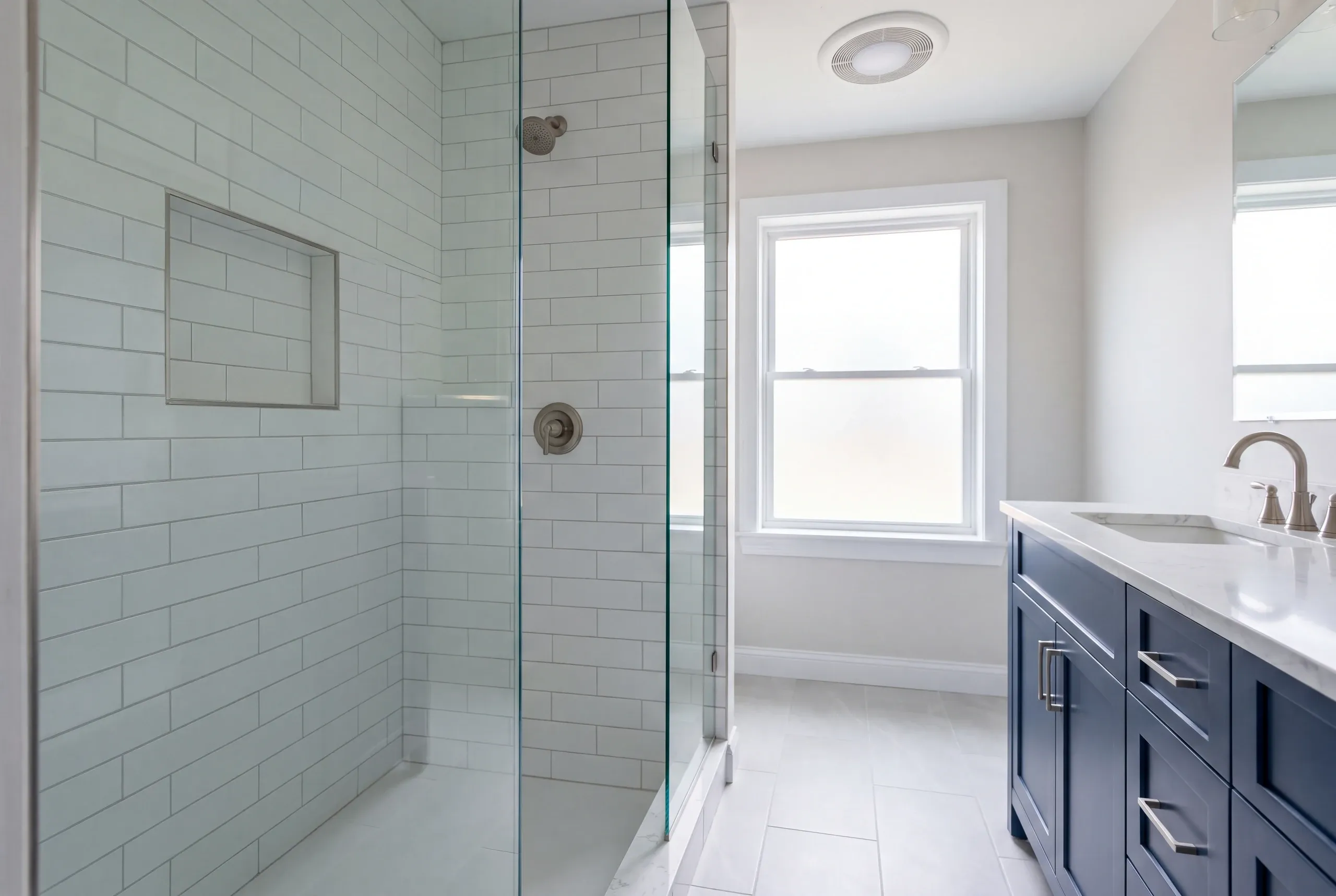 Bathroom renovation contractor Bucksport Maine: glass subway tile shower with a recessed niche beside a navy vanity and frosted window