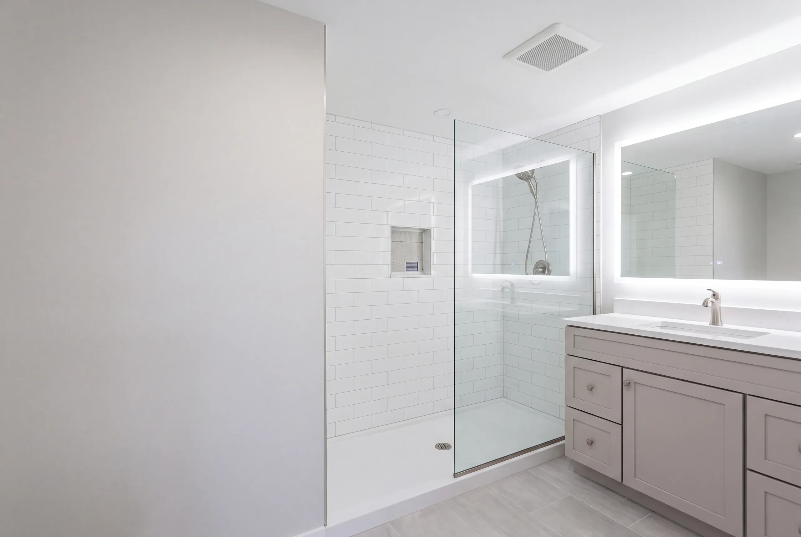 Bathroom remodeler Bucksport Maine: white bathroom with a subway tile shower on a white base and a backlit mirror over a gray vanity