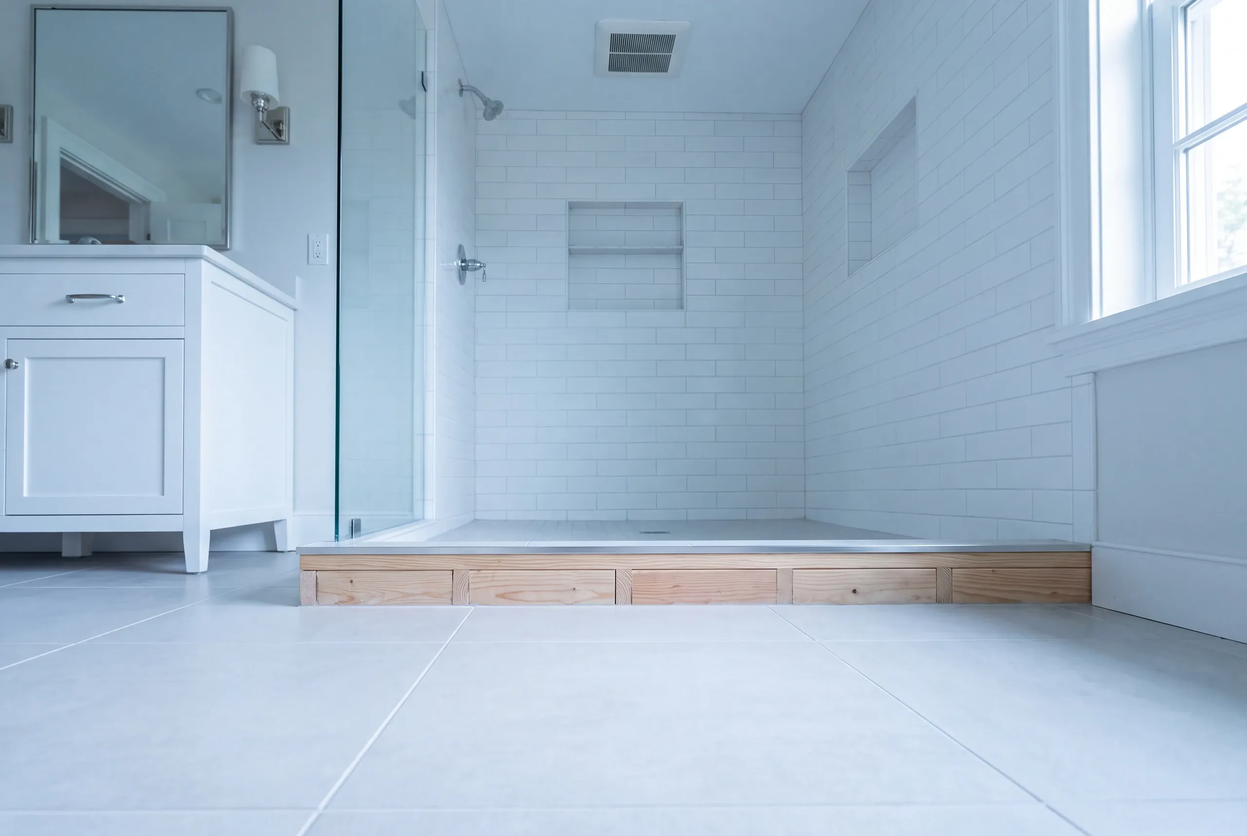 Bathroom renovation contractor Camden Maine: raised shower platform with exposed lumber under the tiled pan beside a white vanity