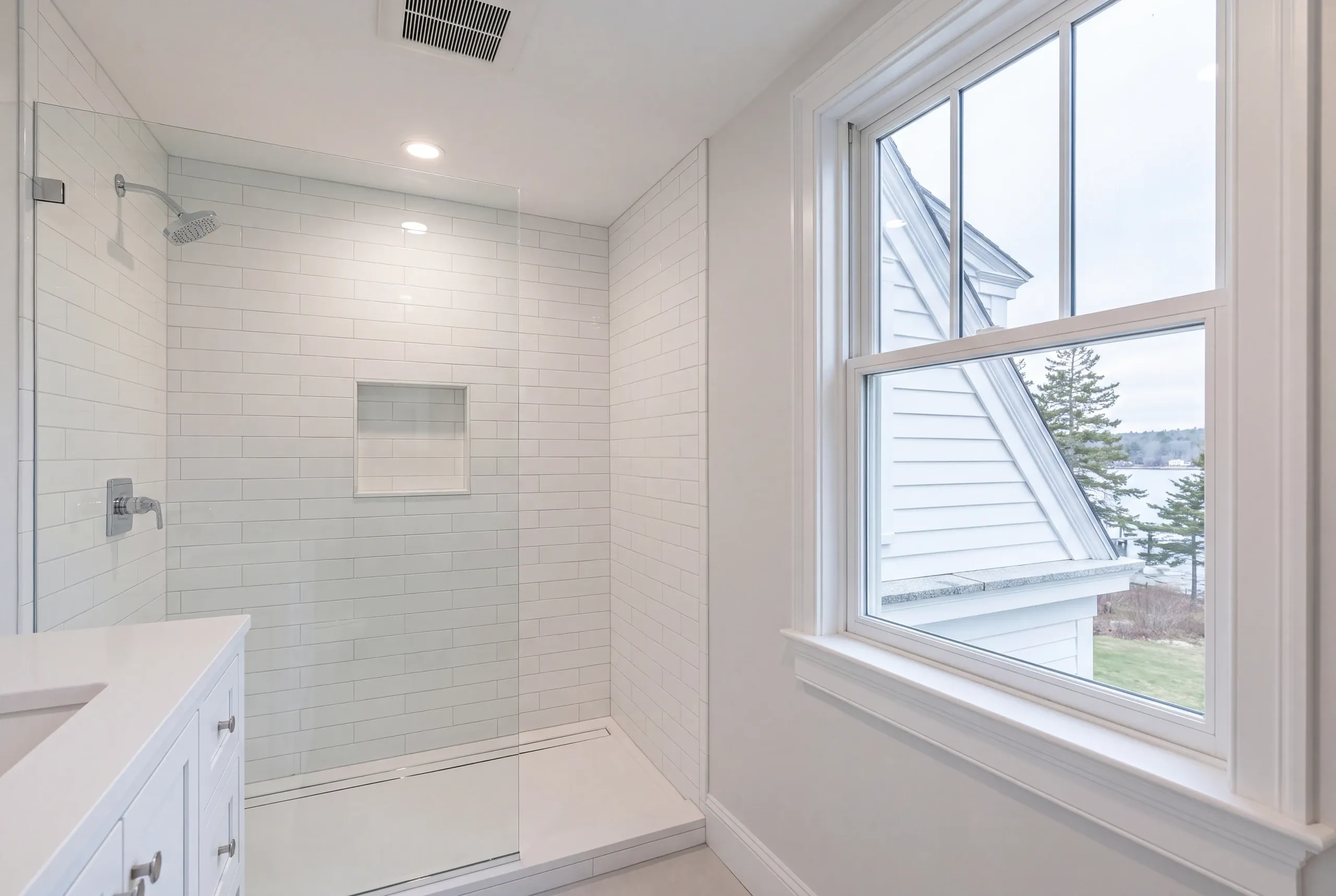 Bathroom remodeler Camden Maine: white subway tile shower with a linear drain and glass panel beside a window over the water