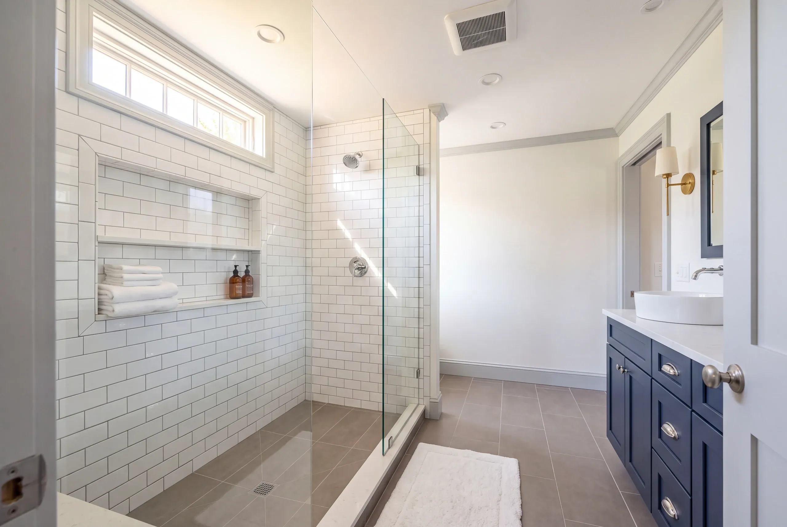 Bathroom remodeling contractor Camden Maine: subway tile shower with a long towel niche under a transom window, navy vanity and vessel sink