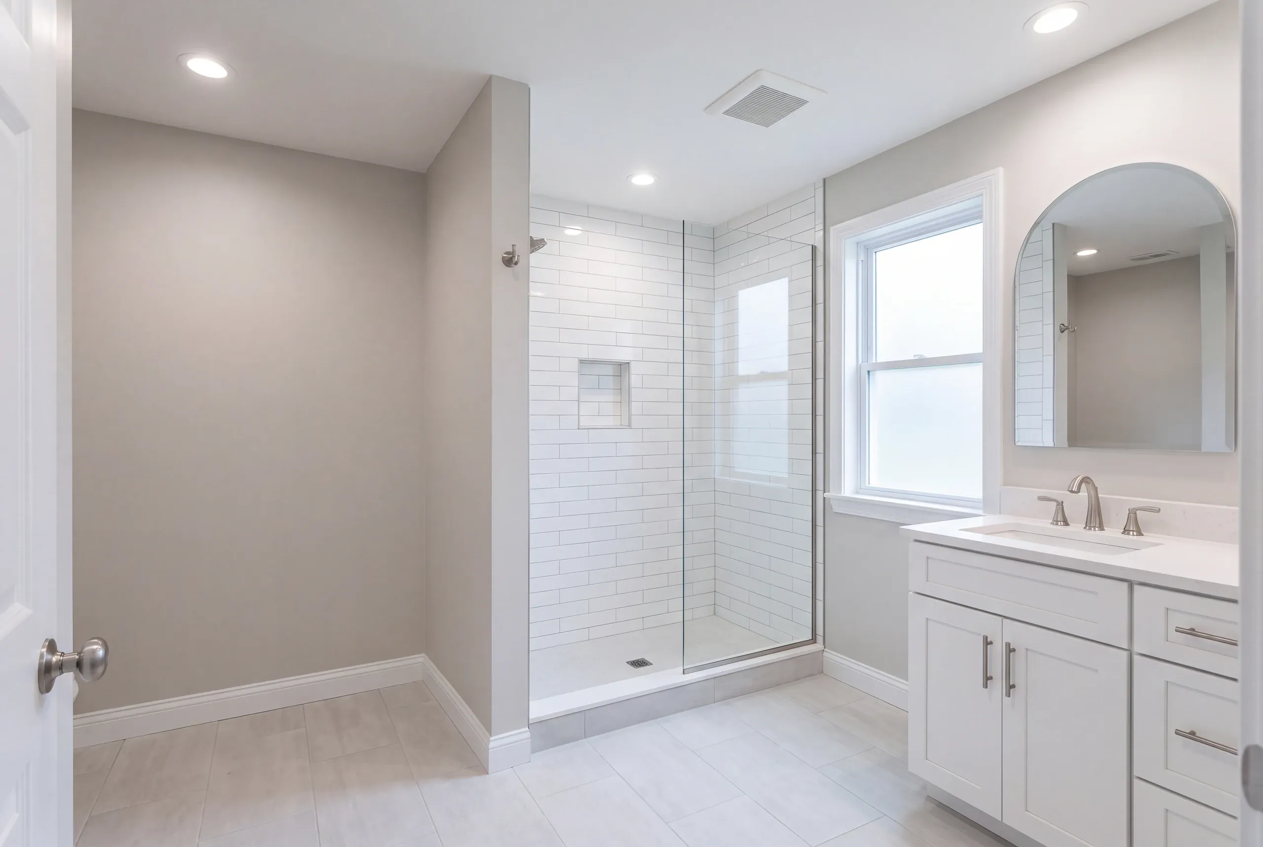 Bathroom renovation contractor Camden Maine: gray-walled bathroom with a white subway tile shower, white shaker vanity and arched mirror