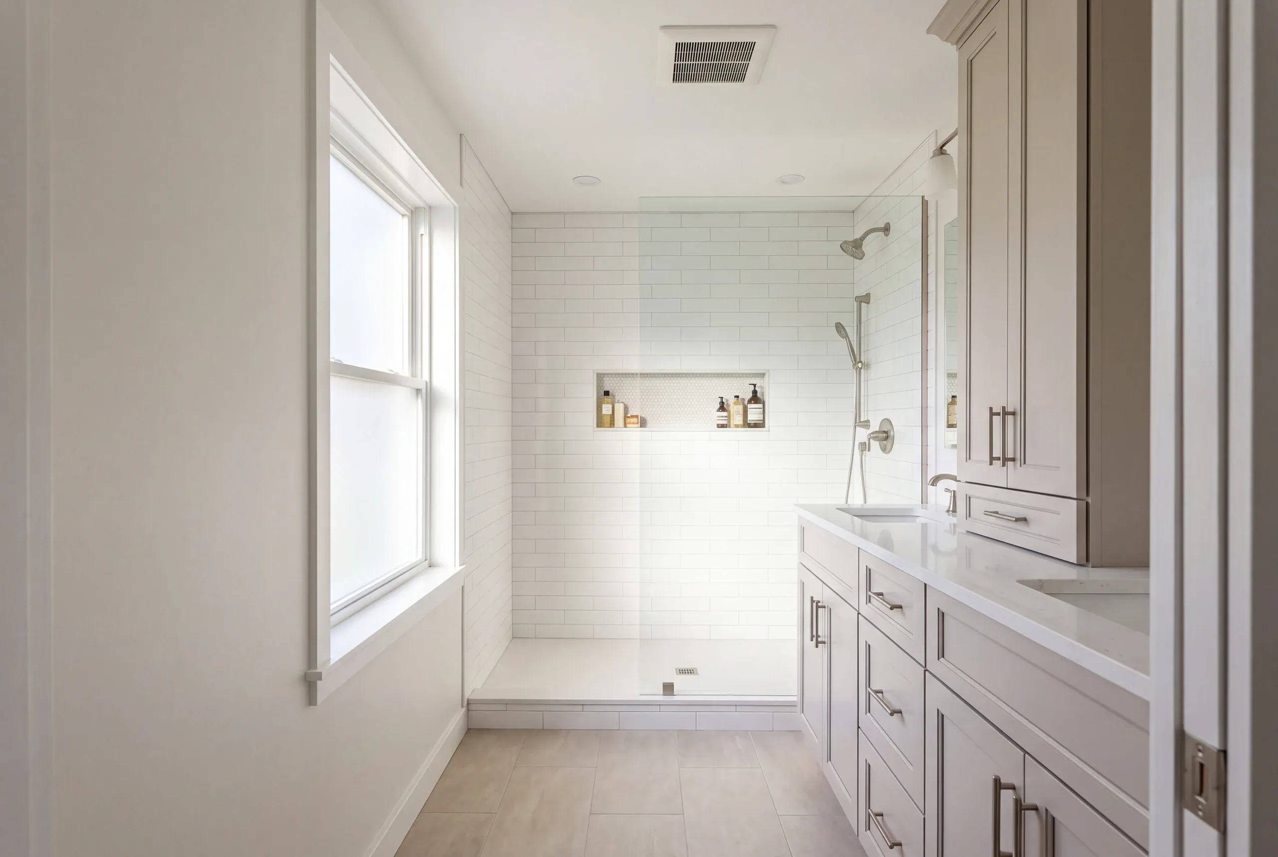 Bathroom remodeling contractor Midcoast Maine: bright bath with a white subway-tile walk-in shower, gray shaker vanity and tall linen cabinet