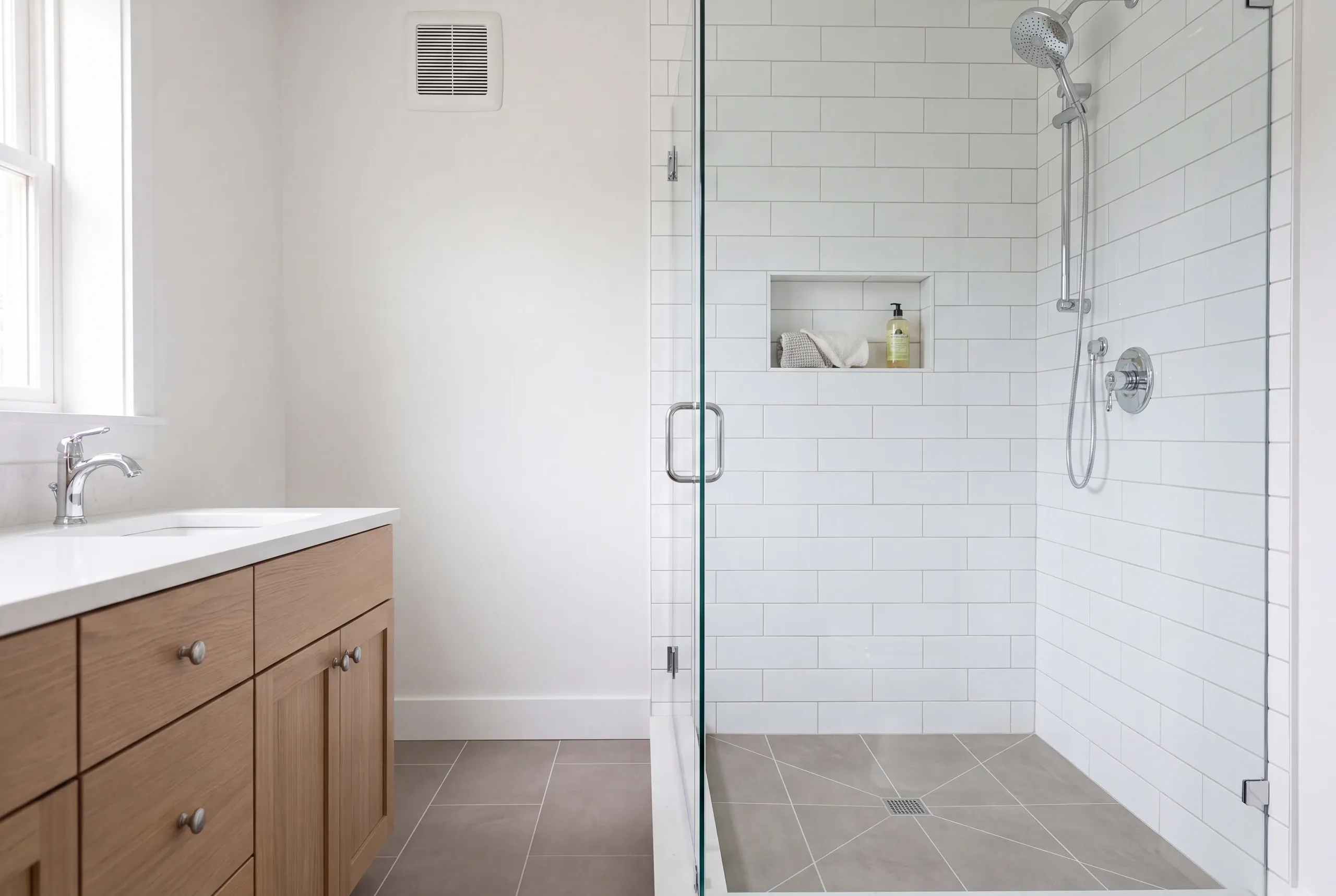 Bathroom renovation contractor Damariscotta Maine: corner glass shower with a handheld spray and towel niche beside a light wood vanity