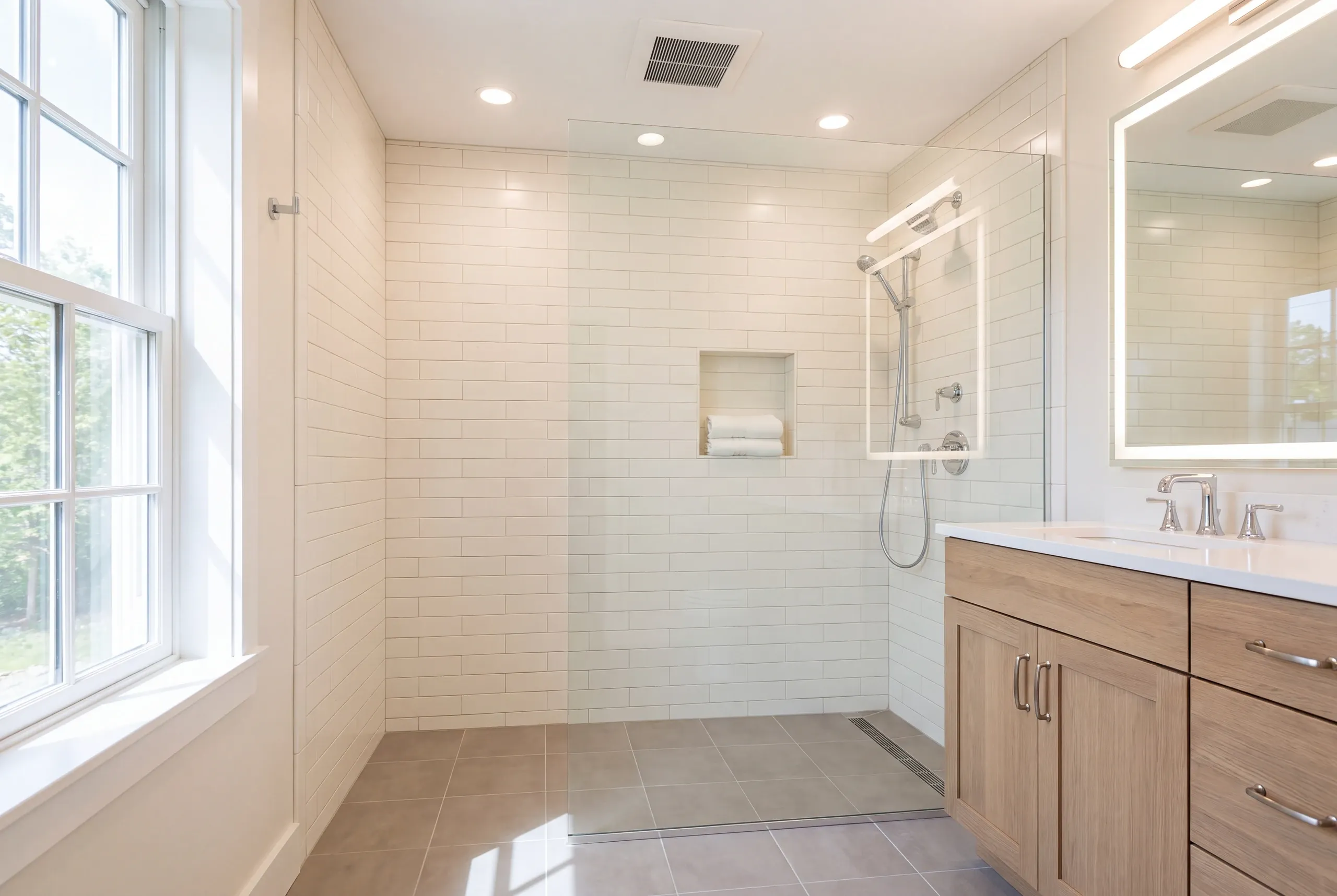Bathroom renovation contractor Damariscotta Maine: curbless walk-in shower with a linear drain, white subway tile and a light wood vanity