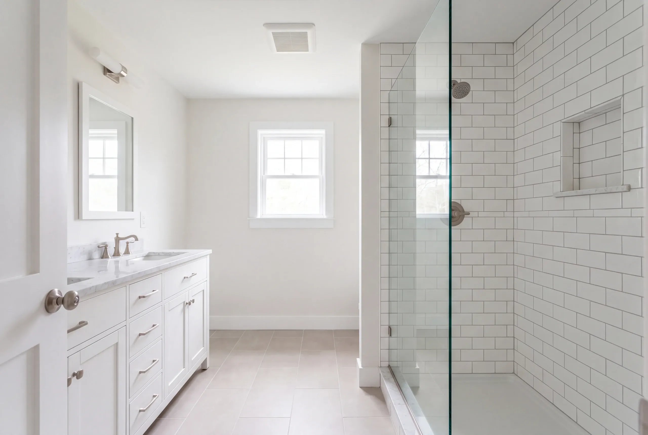 Bathroom remodeler Damariscotta Maine: white bathroom with a stone-top vanity, framed mirror and a glass subway tile shower with niche