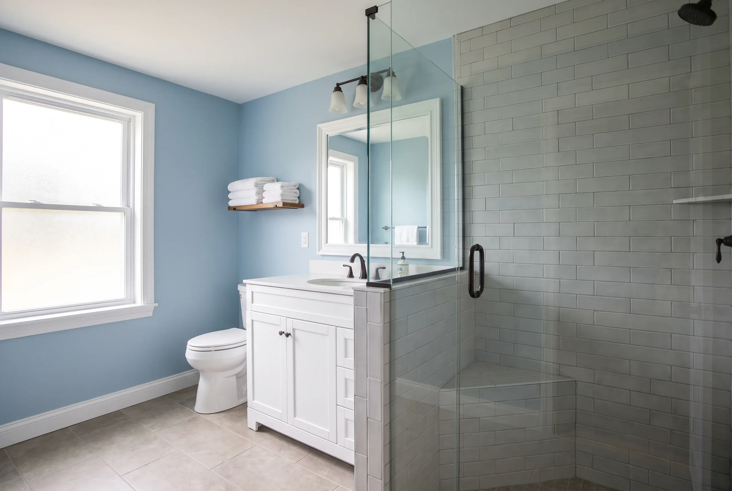 Bathroom remodeling in Fairfield, ME: finished bath with white vanity, toilet and gray subway tile walk-in shower under a bright window