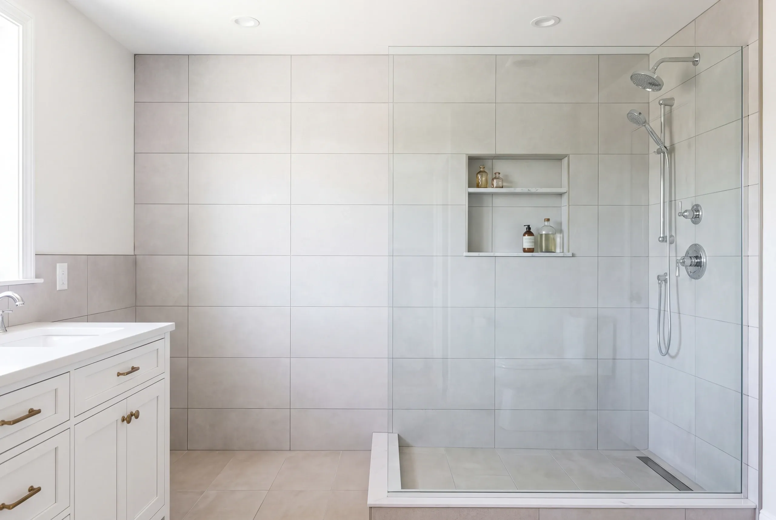 Bathroom renovation contractor Fairfield Maine: light gray large tile shower with a glass enclosure, linear drain and shelf niche