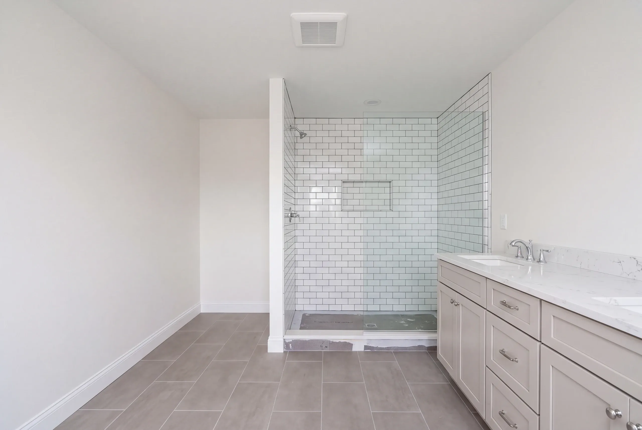 Bathroom renovation contractor Fairfield Maine: bathroom with a dark-grout subway tile shower, untiled shower floor and a long pale vanity