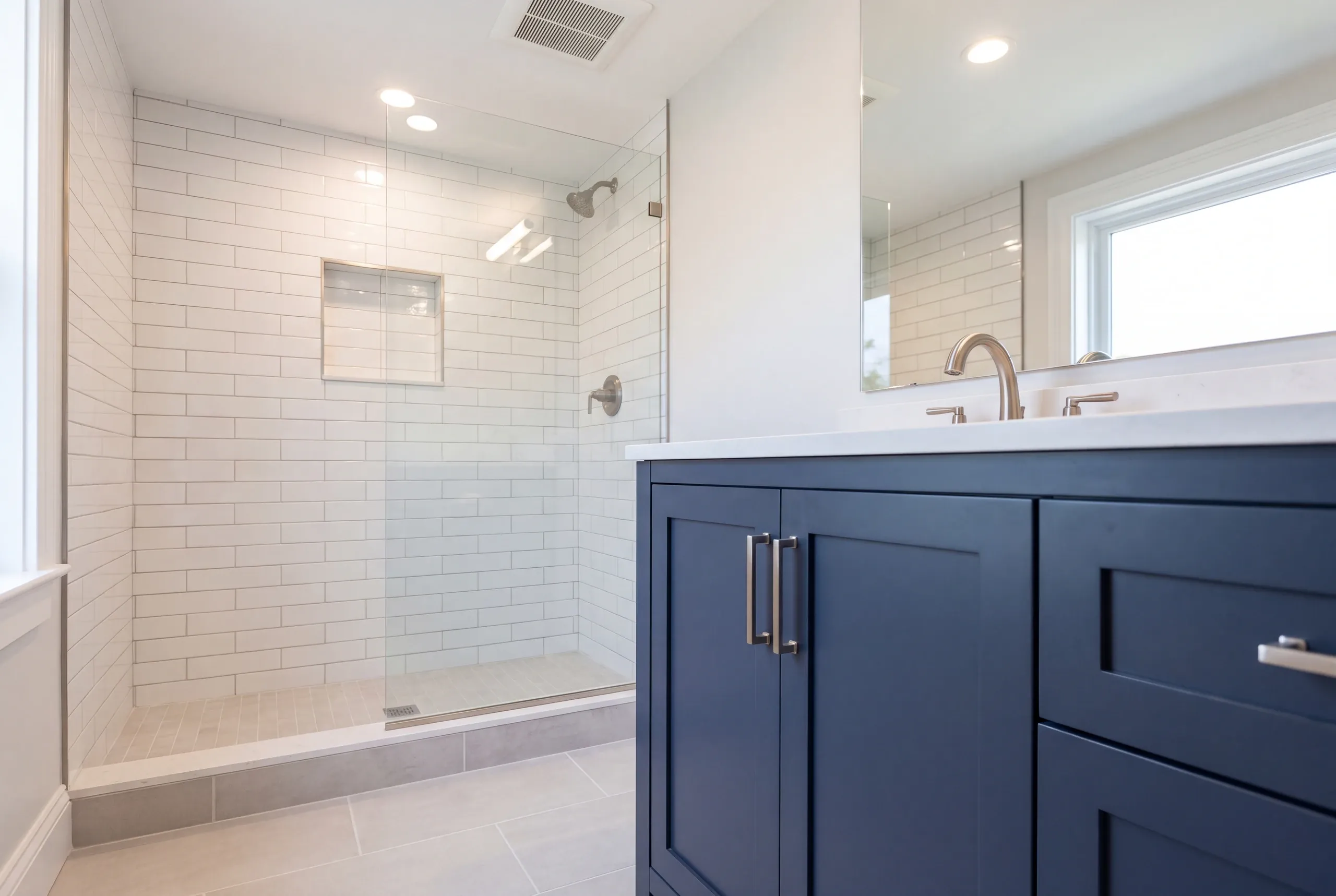 Bathroom renovation contractor Gardiner Maine: white subway tile shower on a low tiled curb with a glass panel and a navy shaker vanity