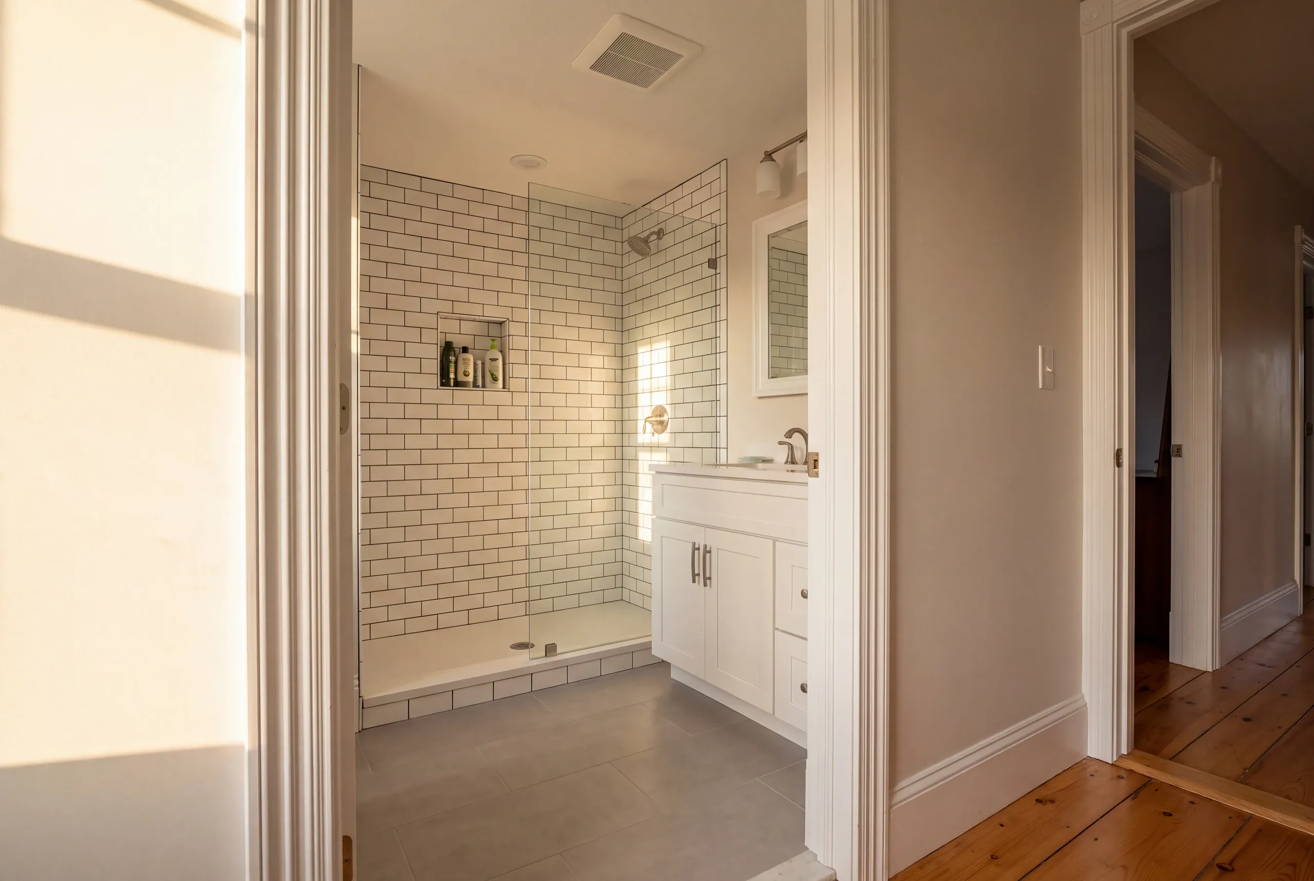 Bathroom remodeler Gardiner Maine: hallway view with wide pine floors into a bath with a dark-grout subway tile shower