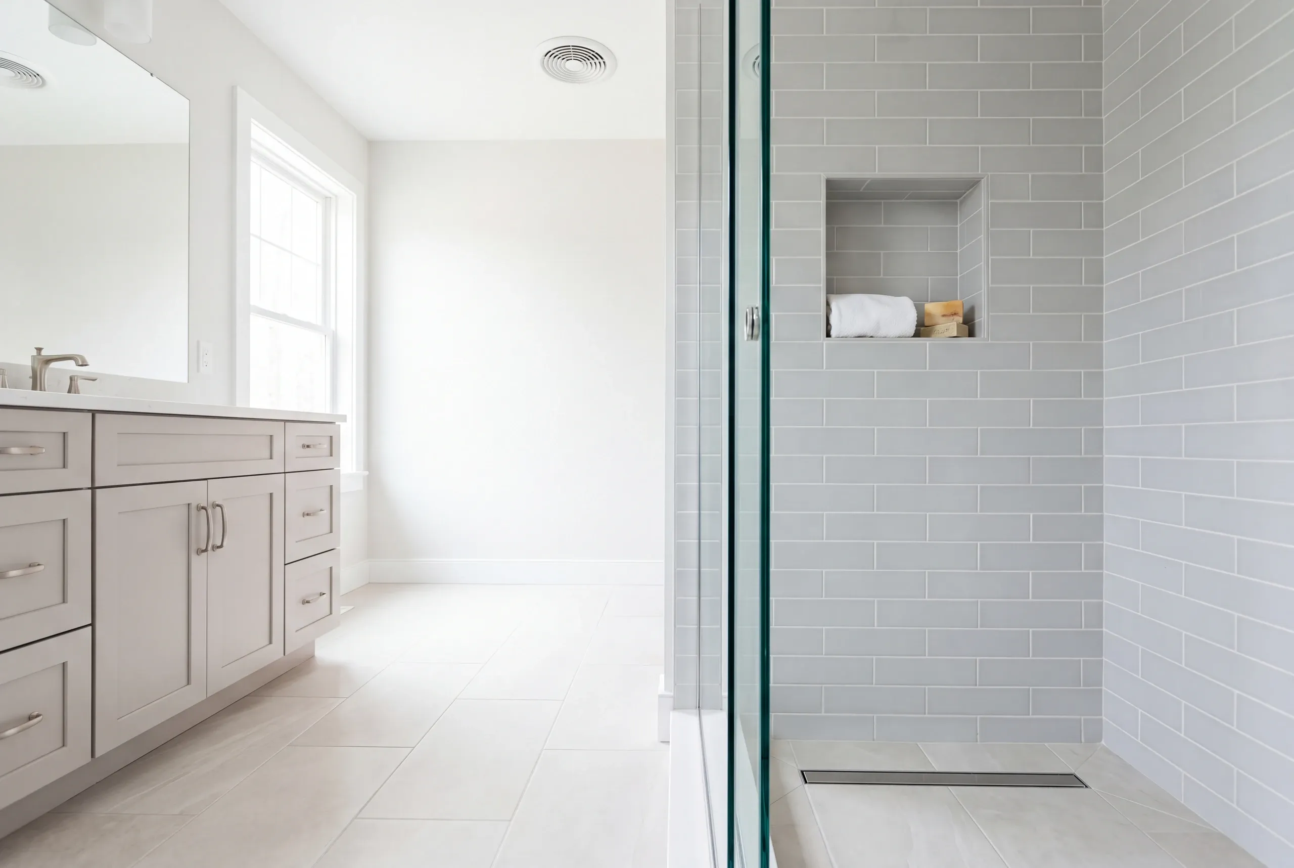 Bathroom renovation contractor Lincolnville Maine: gray subway tile shower with a linear drain and towel niche beside a gray shaker vanity