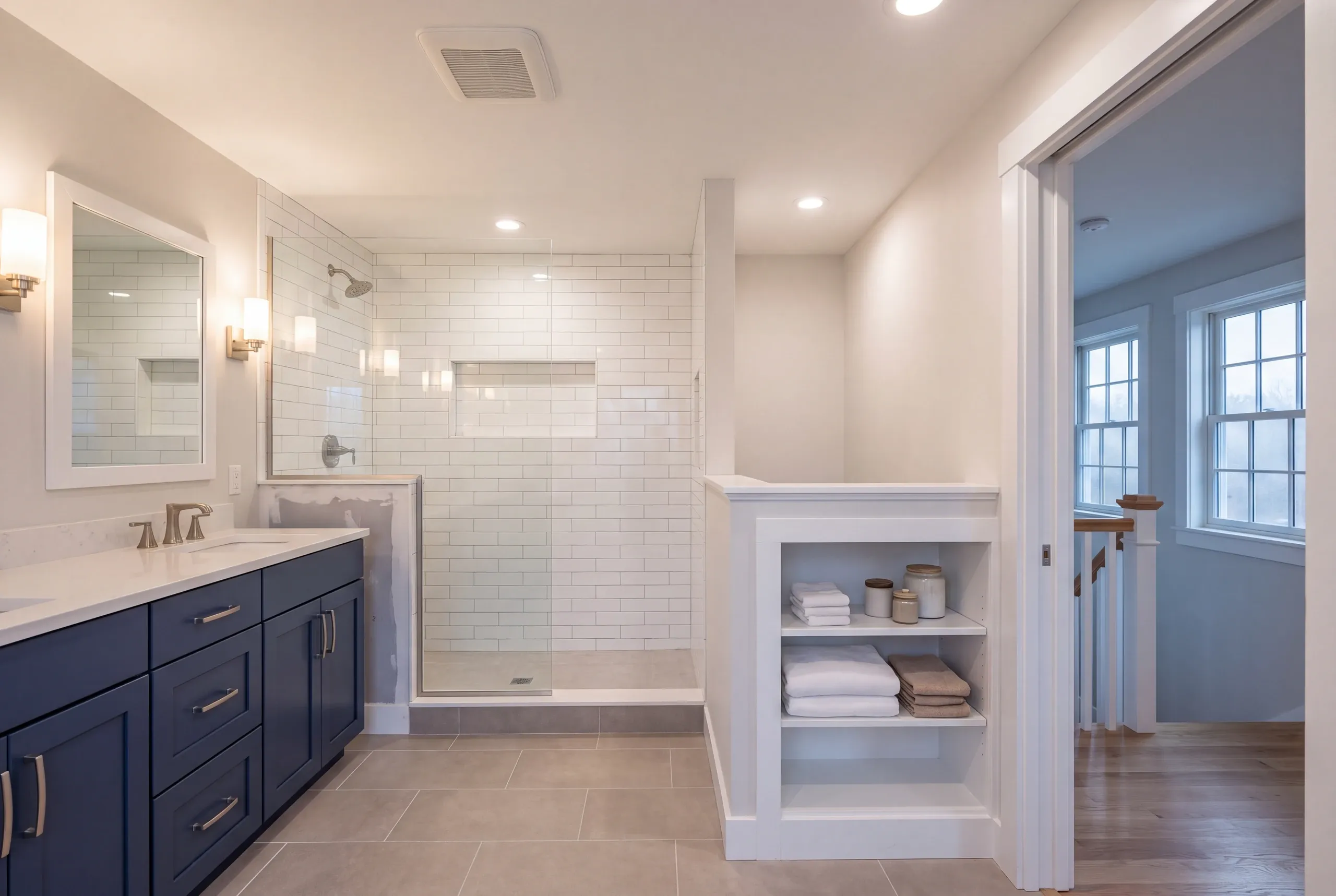 Bathroom remodeler Lincolnville Maine: bathroom with a navy double vanity, subway tile shower and built-in towel shelves by the stairs
