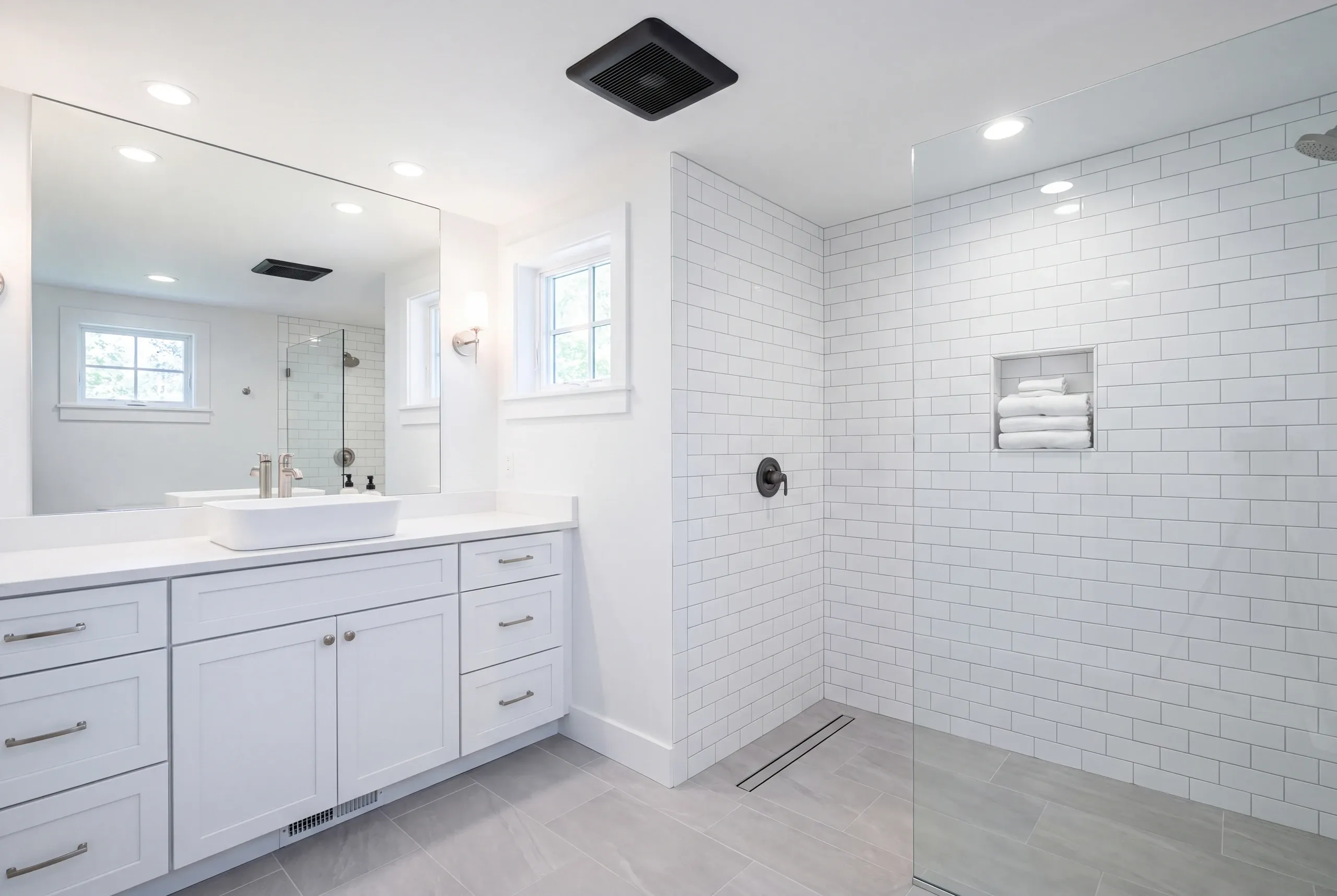 Bathroom renovation contractor Lincolnville Maine: curbless subway tile shower with a matte black valve beside a white vanity with a vessel sink