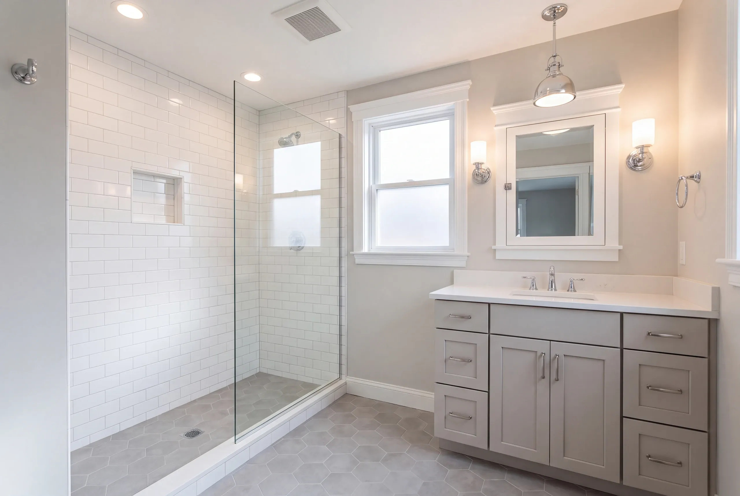 Bathroom remodeling in Pittsfield, ME: bathroom with a subway tile walk-in shower, gray hex floor, gray vanity and pendant light