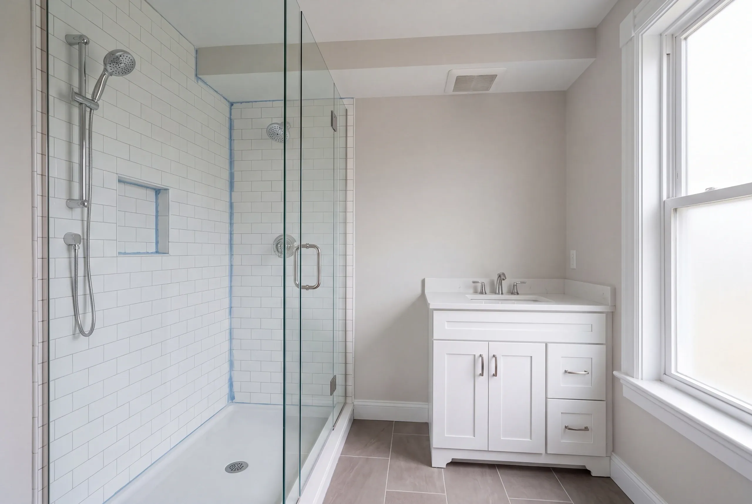 Bathroom remodeling contractor Pittsfield Maine: glass enclosed subway tile shower with a slide bar handheld spray beside a white vanity