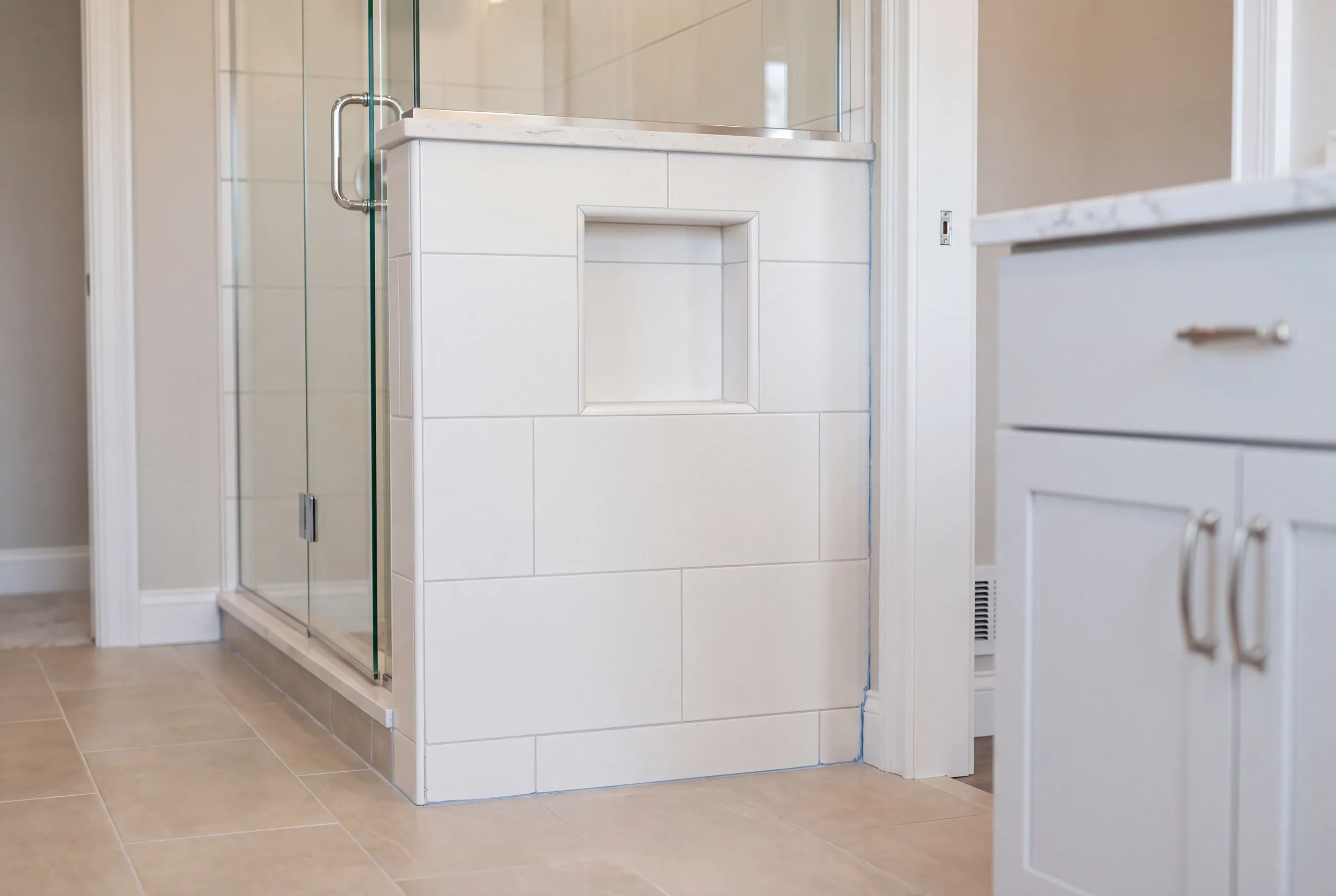 Bathroom renovation contractor Pittston Maine: close view of a tiled shower half wall with a niche, stone-look cap and glass door