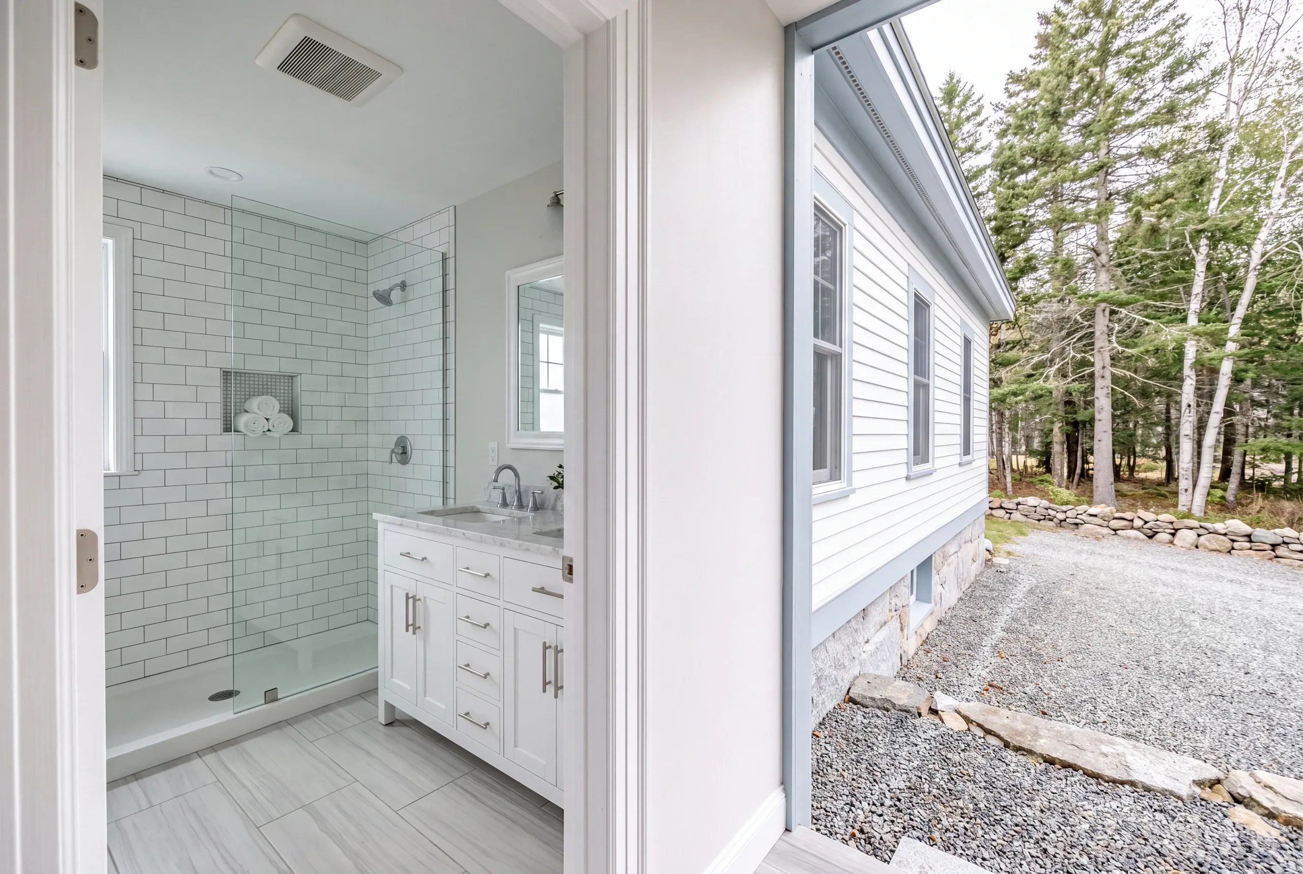Bathroom remodeler Pittston Maine: open bathroom doorway showing a subway tile shower and white vanity off a back entry