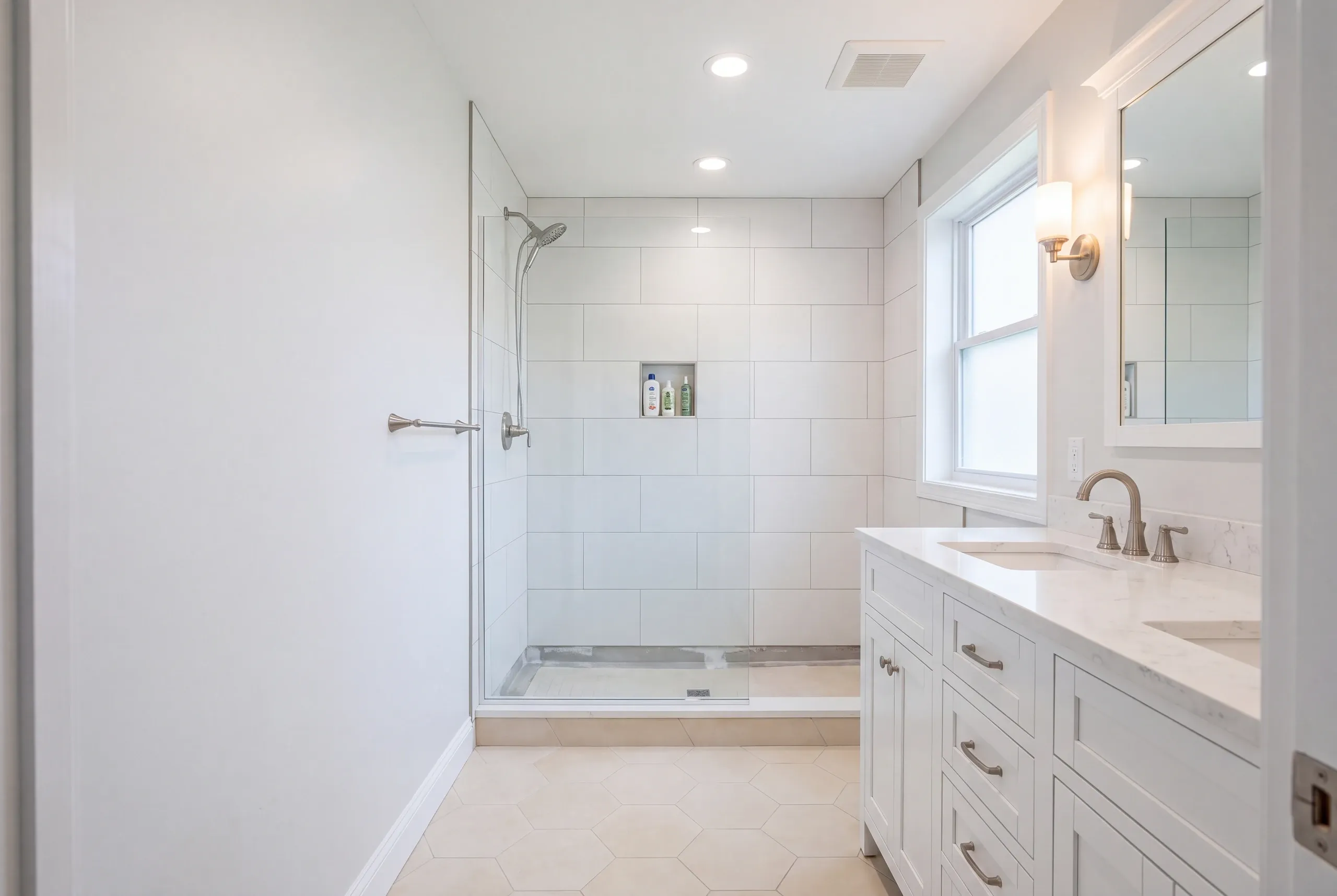 Bathroom remodeler Pittston Maine: white bathroom with a large tile glass shower, hex floor and a white double vanity