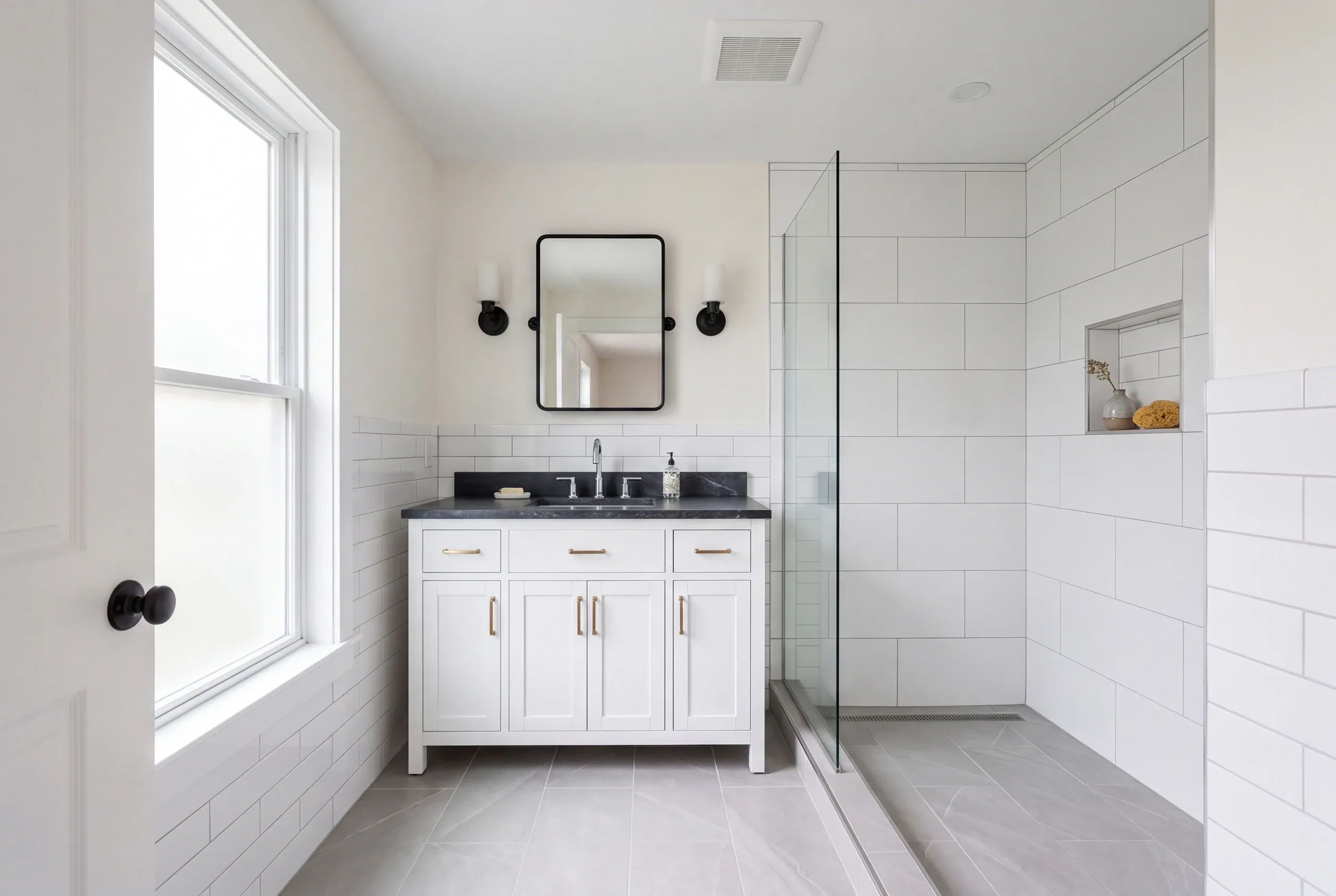 Bathroom remodeler Rockland Maine: white vanity with a black stone top and black mirror beside a curbless walk-in shower