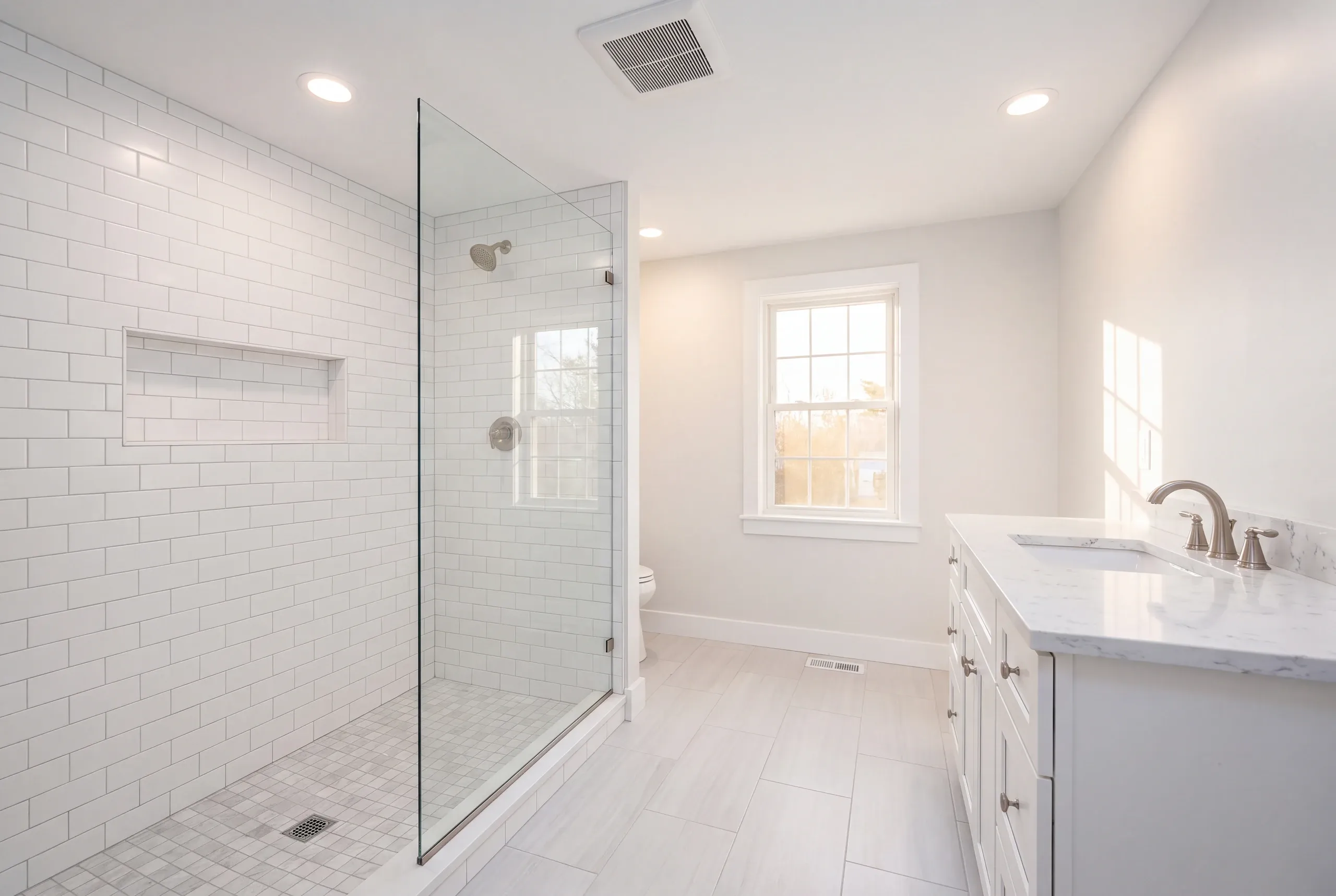 Bathroom remodeling in Rockport, ME: white subway tile shower with a long niche and gray mosaic floor beside a white vanity