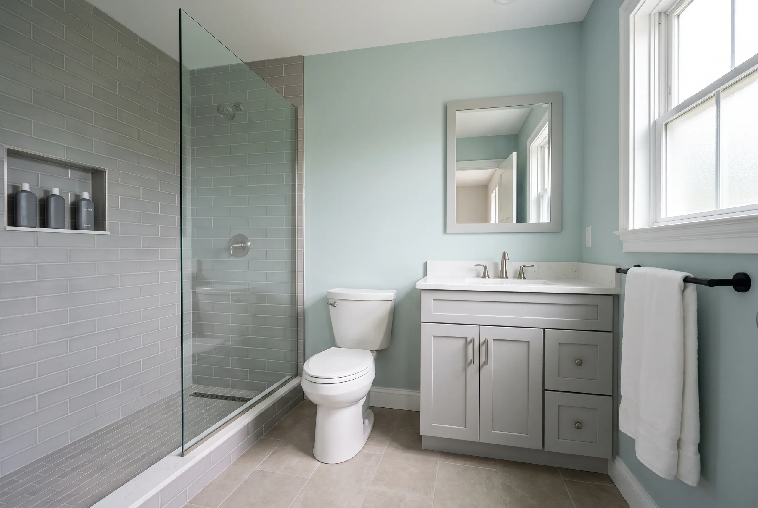 Bathroom remodeling contractor Rockport Maine: light gray subway tile walk-in shower with a niche beside a gray vanity and toilet