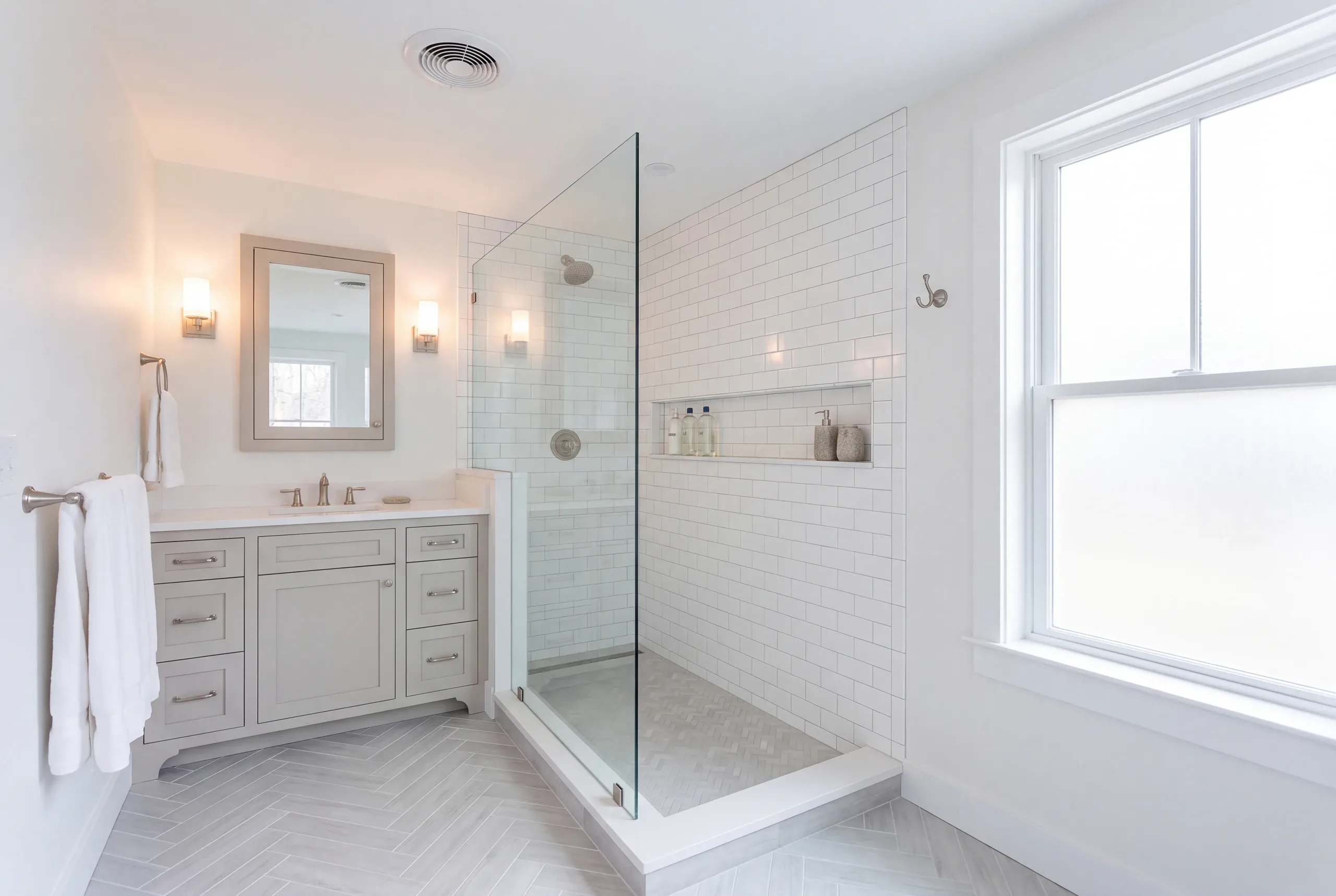 Bathroom renovation contractor Rockport Maine: herringbone floor bathroom with a gray vanity and a subway tile shower with a long niche