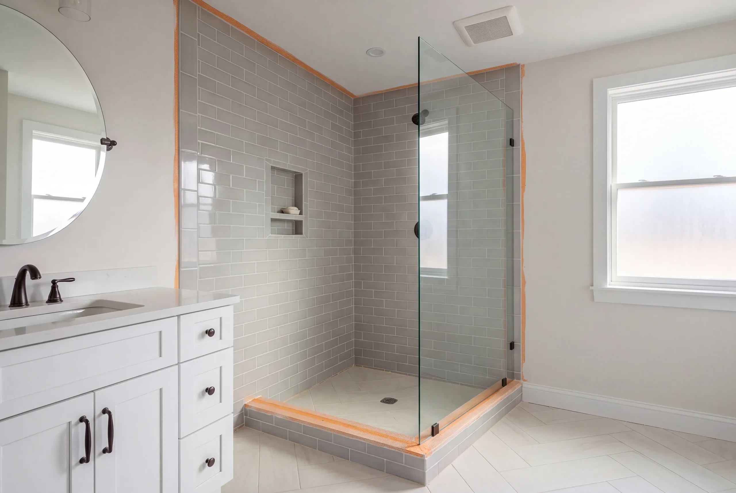 Bathroom renovation contractor Searsmont Maine: gray subway tile corner shower with orange membrane edges still showing and a round mirror