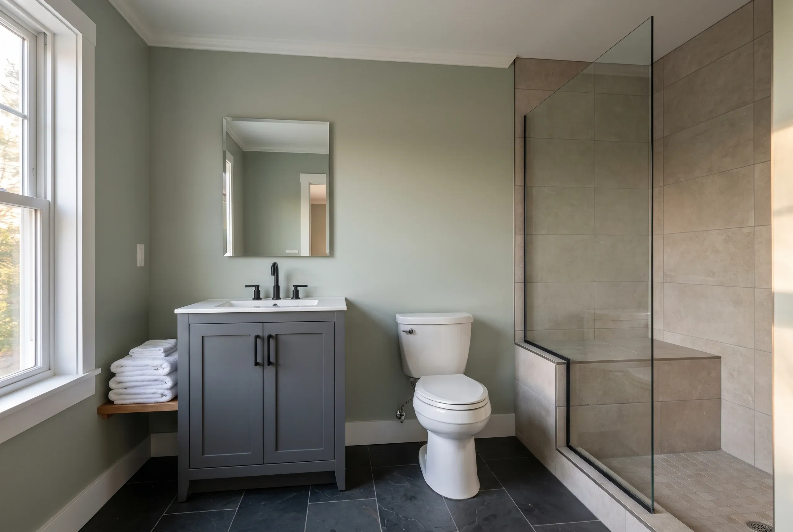 Bathroom remodeling contractor Thomaston Maine: gray vanity and toilet beside a glass walk-in shower with tan large-format tile and bench