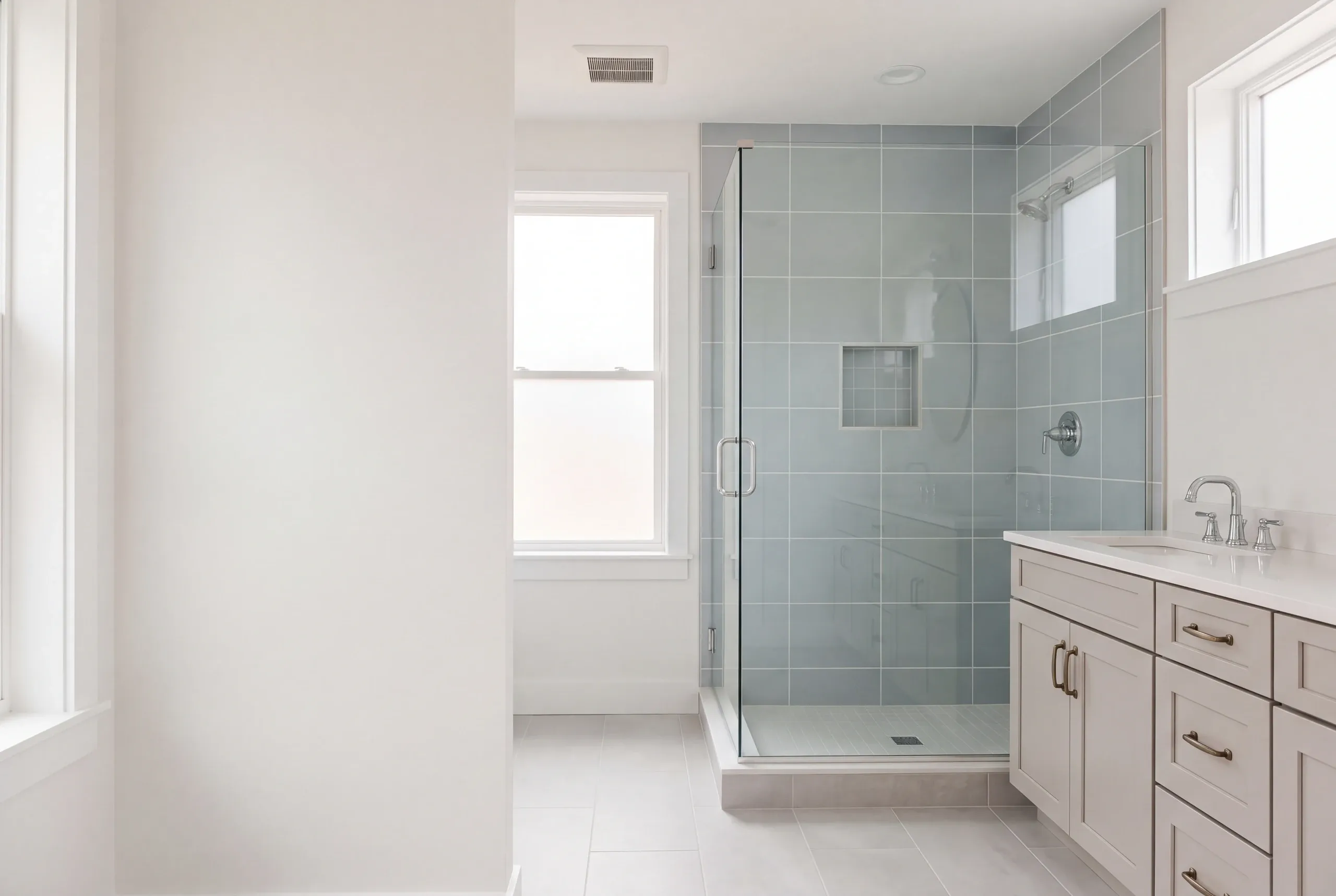 Bathroom remodeler Thomaston Maine: blue-gray tile glass corner shower beside a gray shaker vanity and two windows