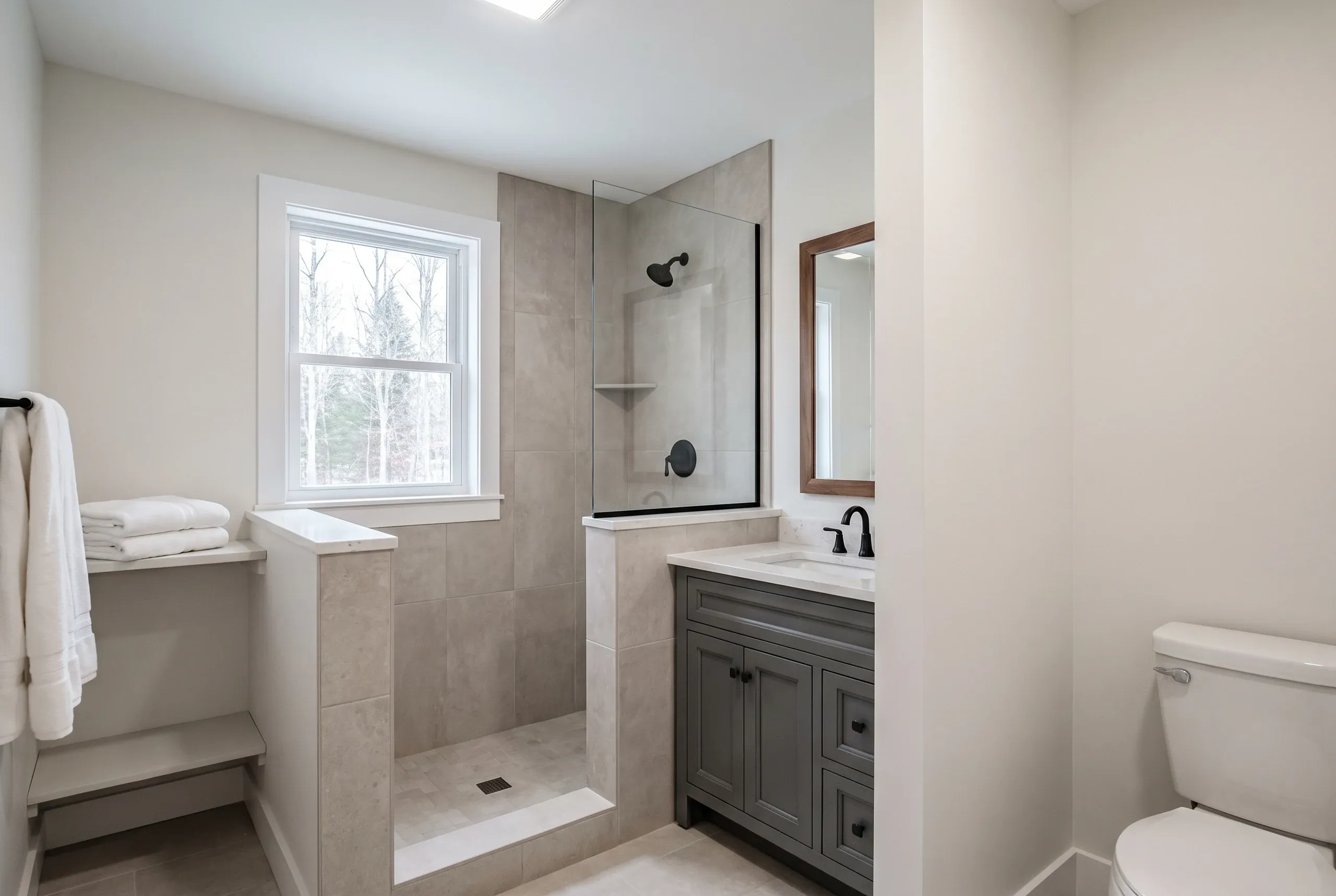 Bathroom remodeling in Waldoboro, ME: finished bath with tile walk-in shower, gray vanity and half-wall beside a window