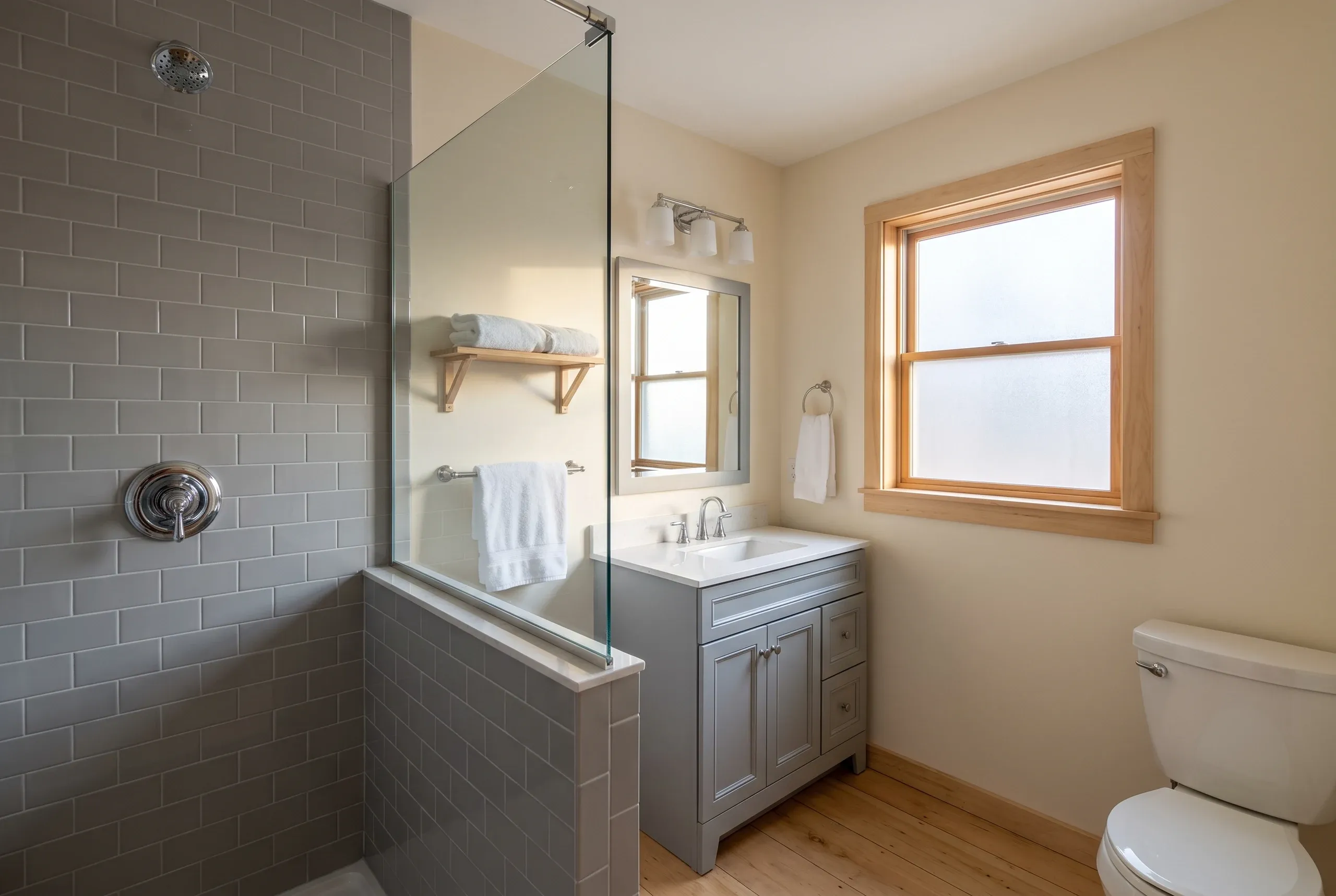 Bathroom remodeling contractor Waldoboro Maine: gray subway tile shower with glass panel beside a gray vanity and wood floor