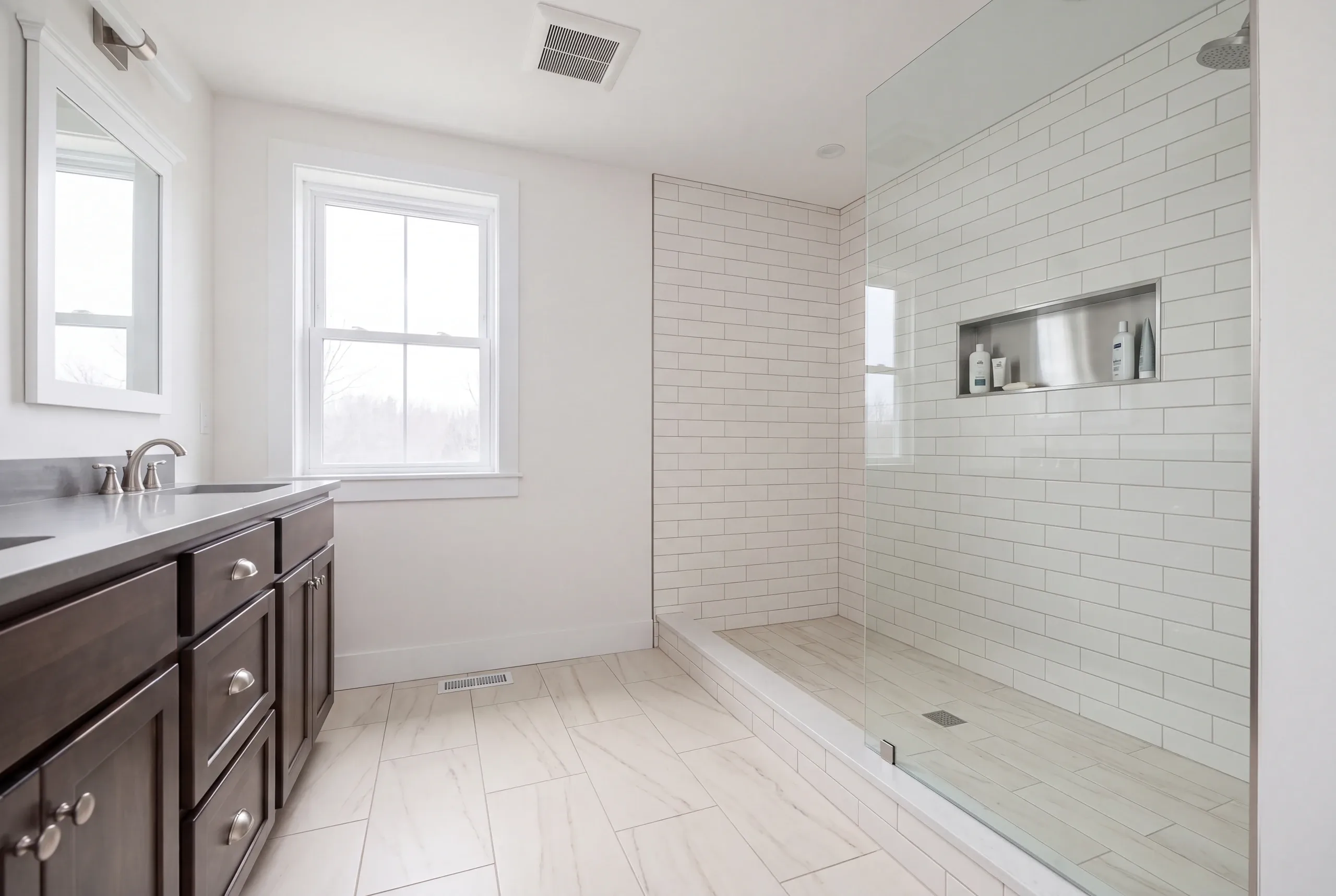 Bathroom renovation contractor Waldoboro Maine: white subway tile walk-in shower with a stainless niche beside a dark wood vanity
