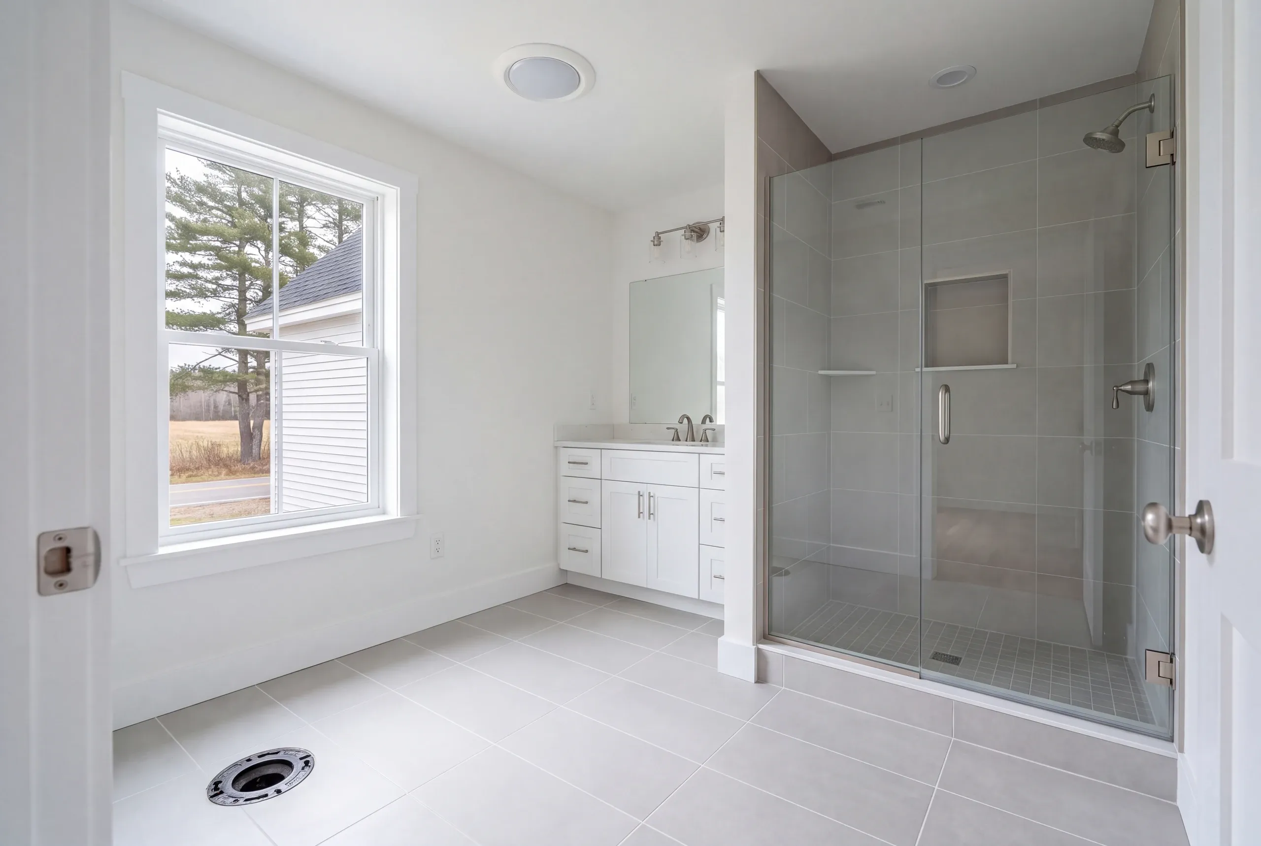 Bathroom remodeler Warren Maine: toilet flange set in a finished tile floor with a glass shower and white vanity beyond