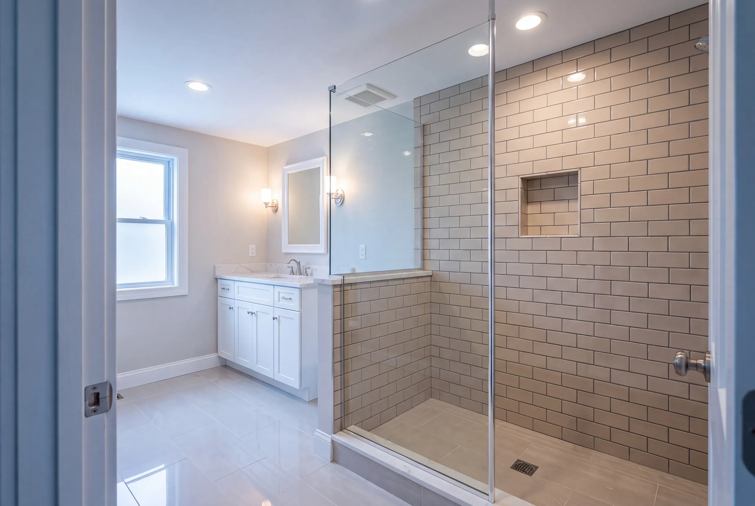 Bathroom remodeling in Waterville, ME: greige subway tile walk-in shower with a glass panel and niche beside a white vanity