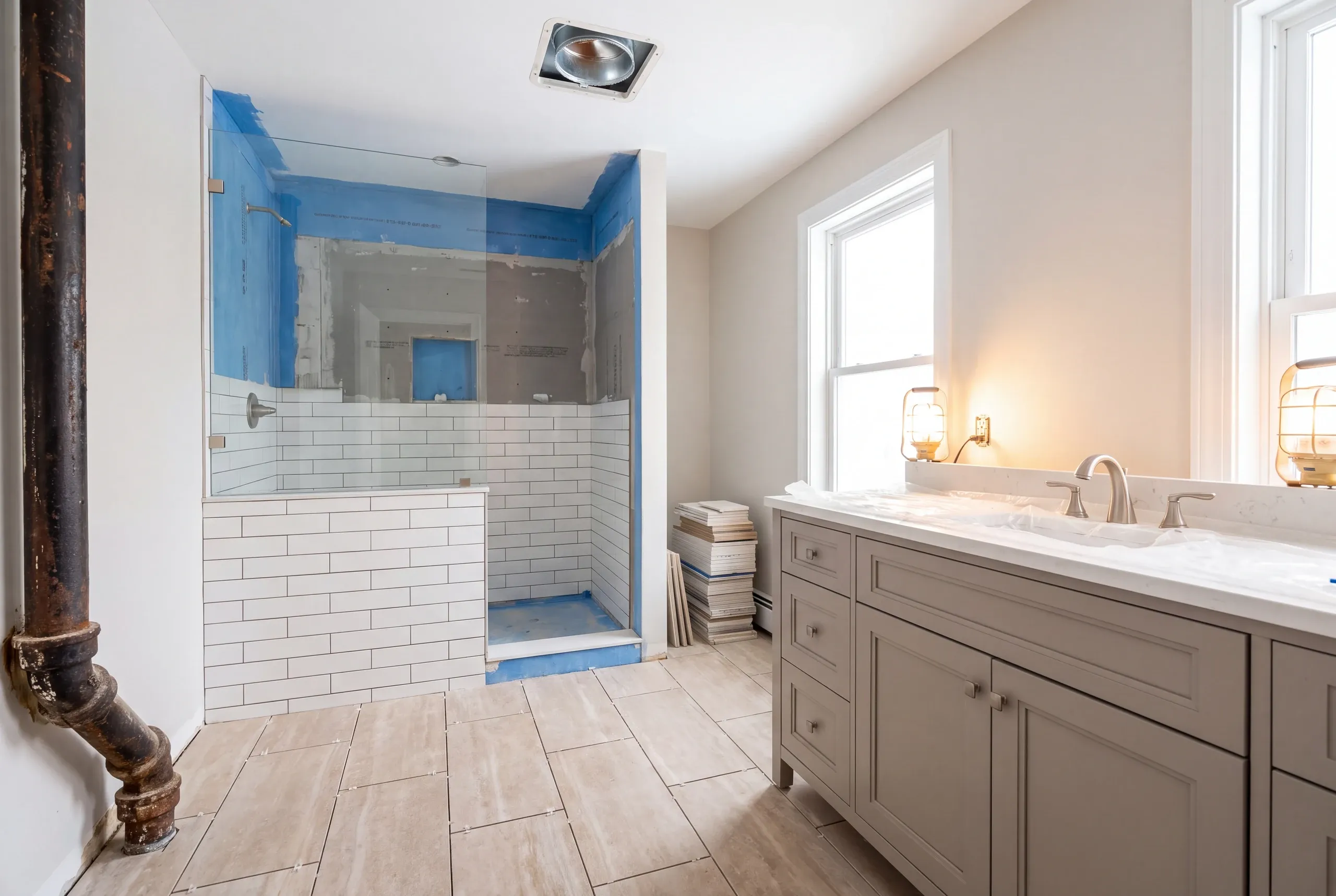 Bathroom remodeling contractor Waterville Maine: corroded cast iron drain on the wall beside a shower half tiled over blue membrane