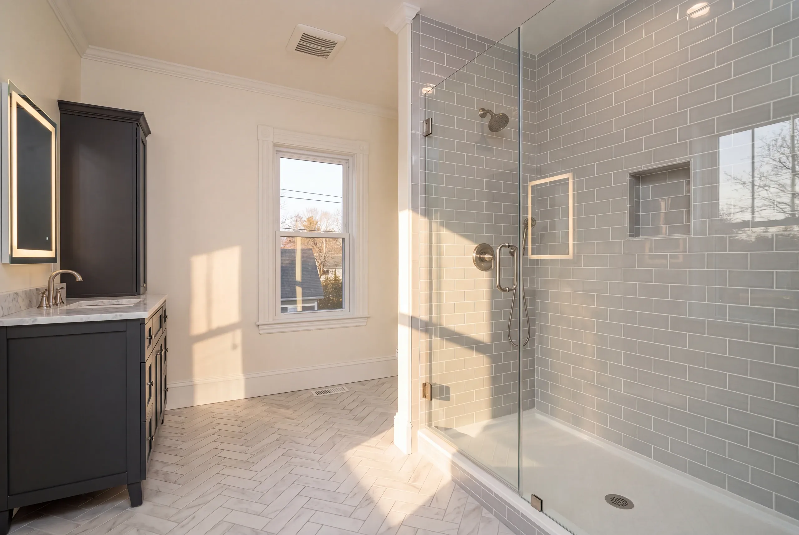 Bathroom renovation contractor Waterville Maine: gray subway tile glass shower beside a charcoal vanity, tall cabinet and herringbone floor