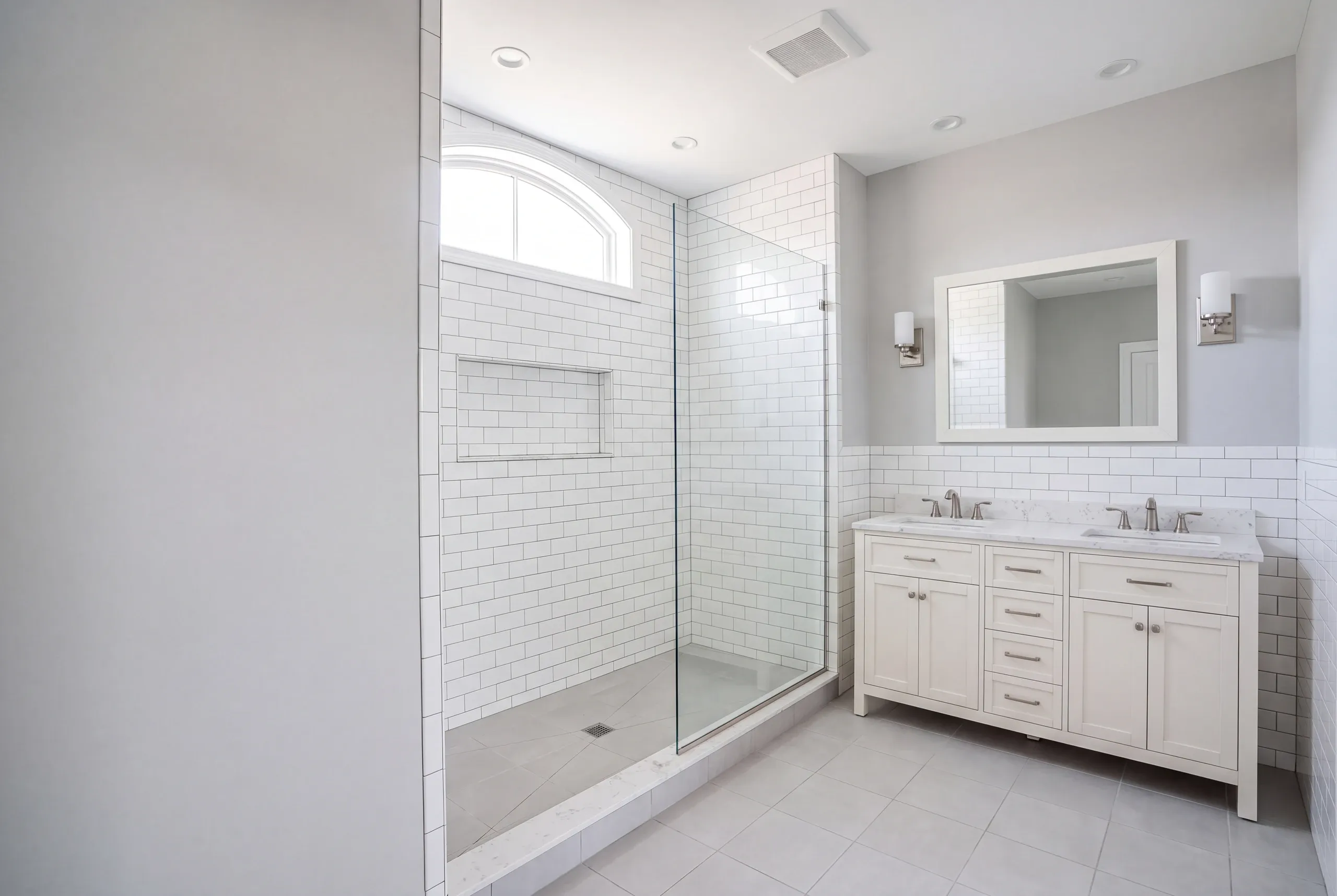 Bathroom remodeler Waterville Maine: shower with an arched transom window and subway tile beside a white double vanity