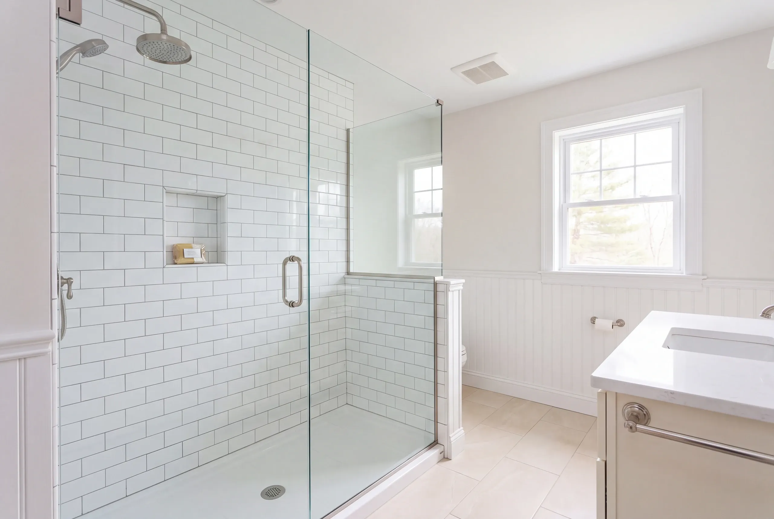 Bathroom remodeling in Windsor, ME: subway tile glass shower with a rain head and handheld spray beside beadboard wainscot