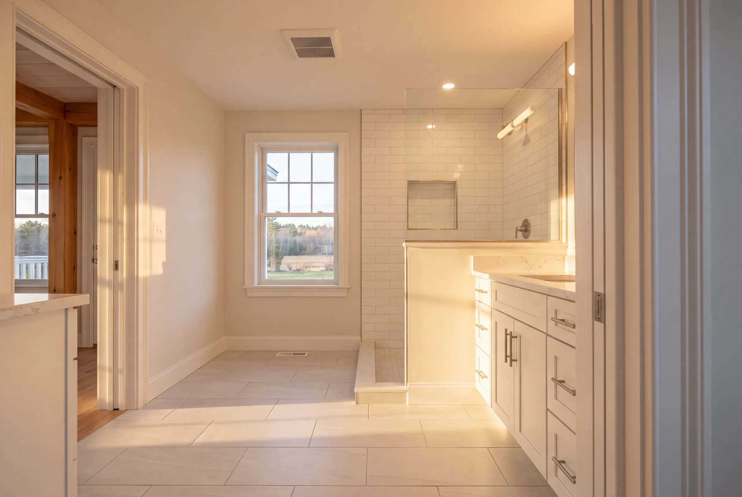 Bathroom remodeler Windsor Maine: sunlit bathroom with large light floor tile, a white vanity and a shower behind a half wall