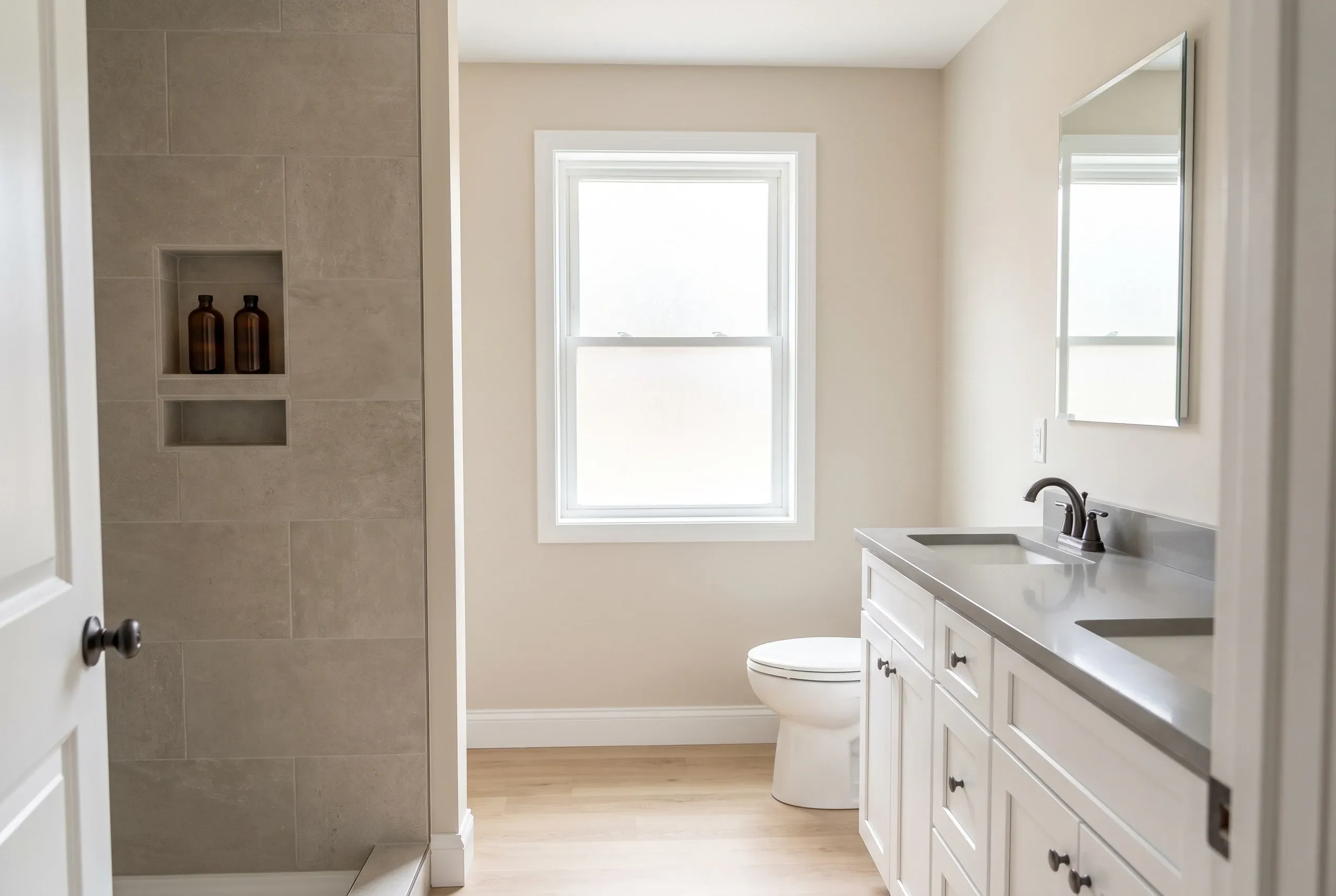 Bathroom remodeling in Winslow, ME: greige tile shower with a two-shelf niche, a toilet under a frosted window and a white double vanity