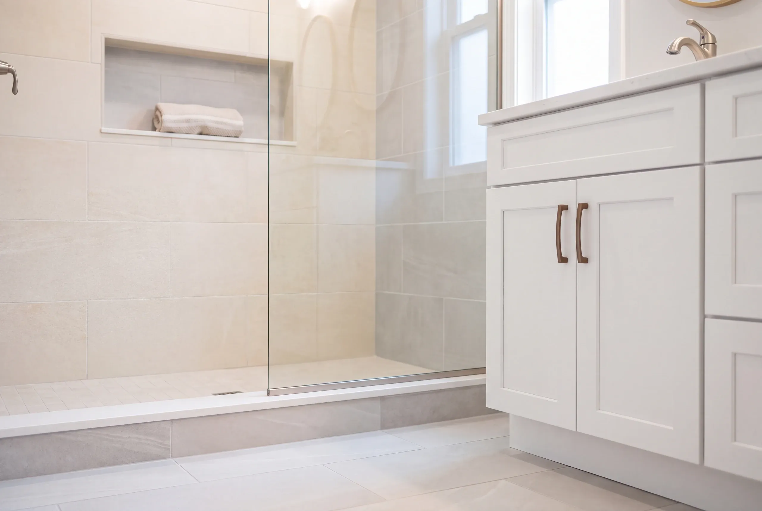 Bathroom renovation contractor Winslow Maine: cream large tile shower with a long towel niche and glass panel beside a white vanity