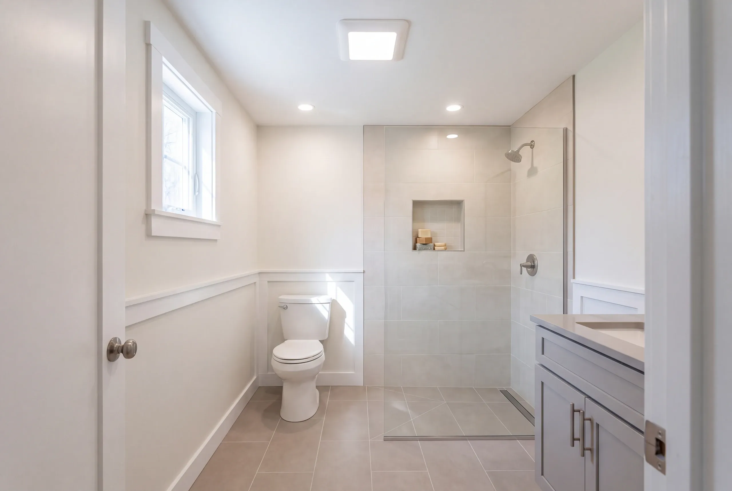 Bathroom remodeling contractor Winslow Maine: curbless large tile shower with a linear drain, toilet, wainscot and lit square ceiling fan