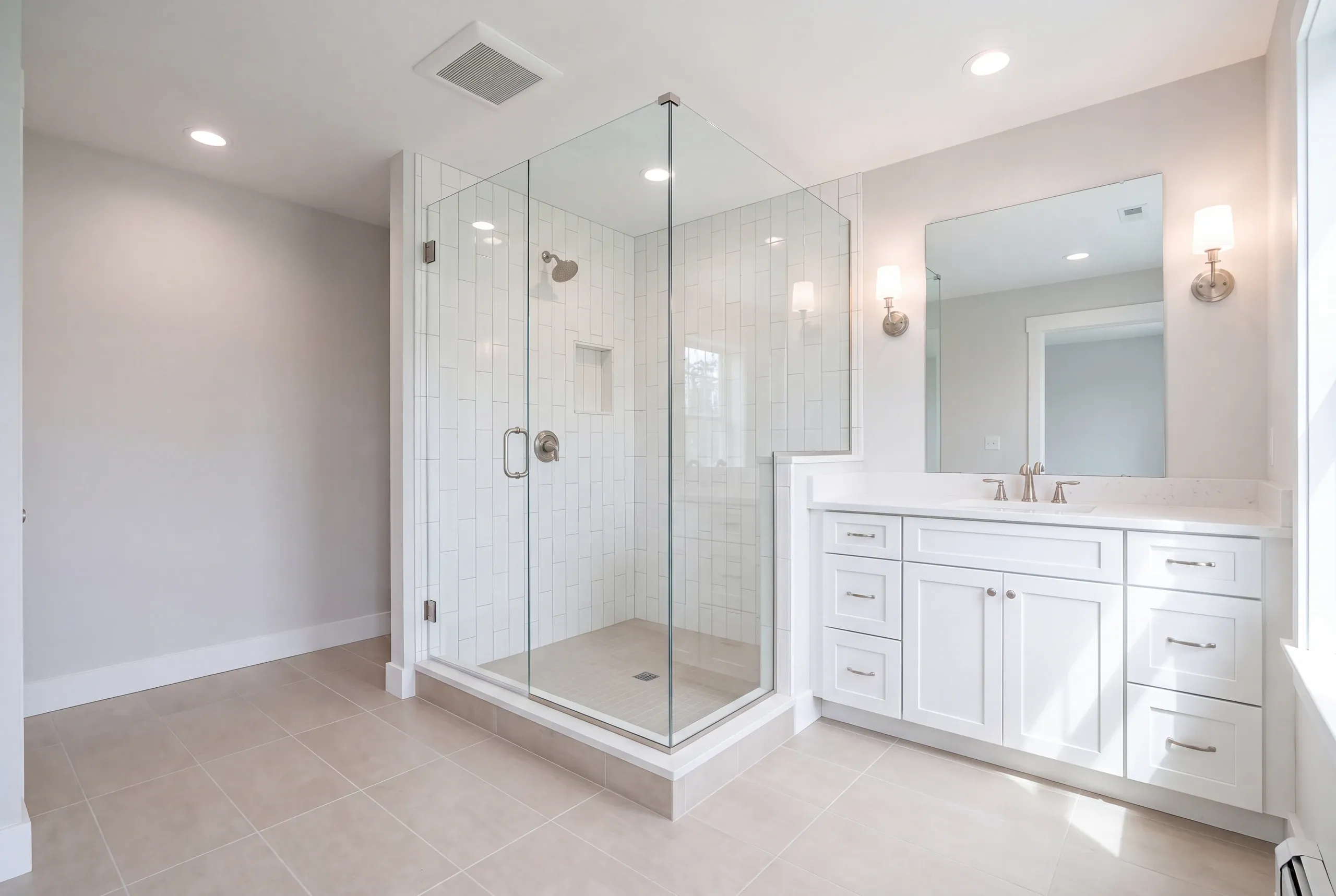 Bathroom remodeler Winslow Maine: glass corner shower with vertical subway tile on a raised base beside a white vanity