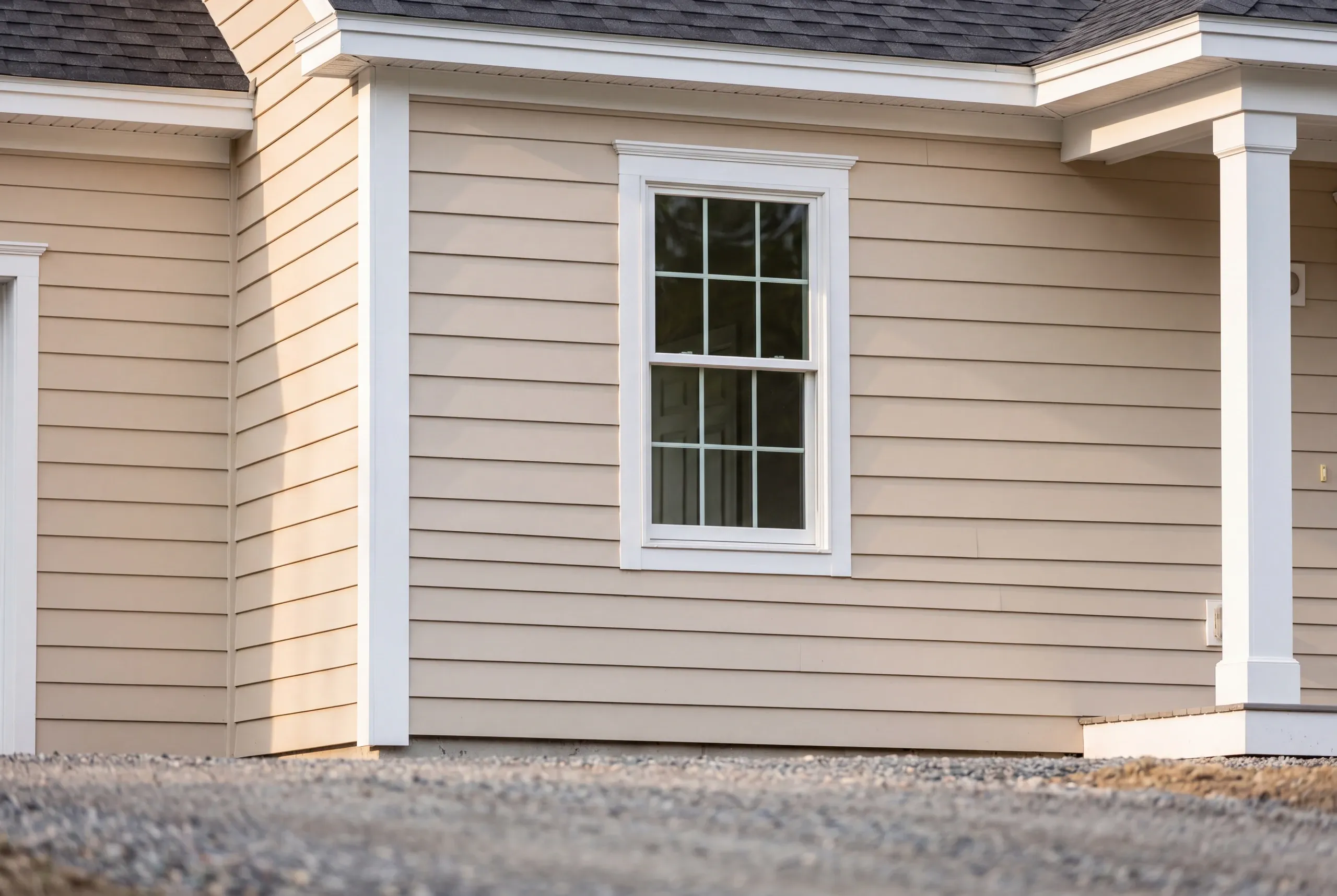 New home builder Belfast Maine: close view of beige lap siding, a white double-hung window and a square white porch column